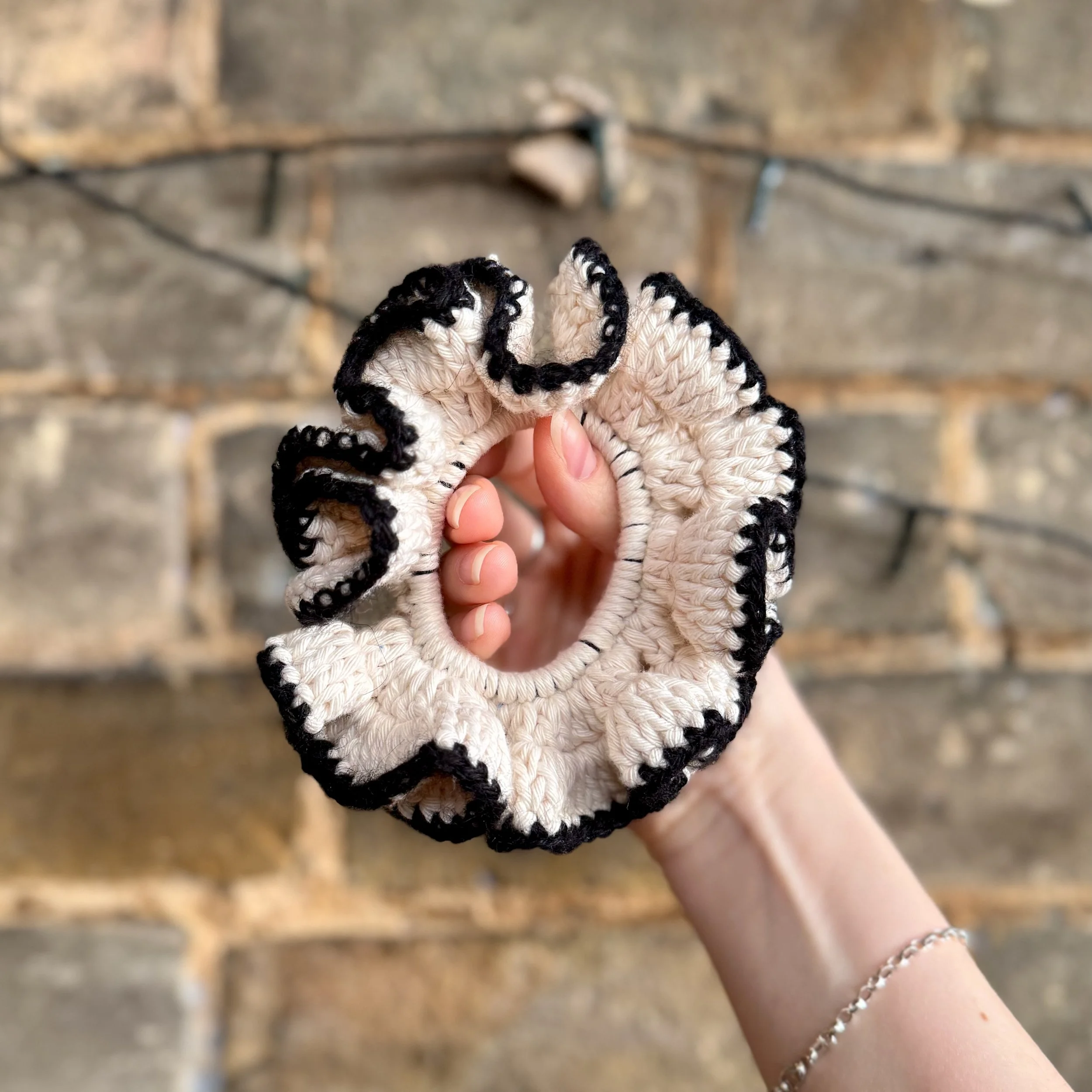 A cream cotton crochet ruffle scrunchie with a black alpaca trim being held to show the ruffles