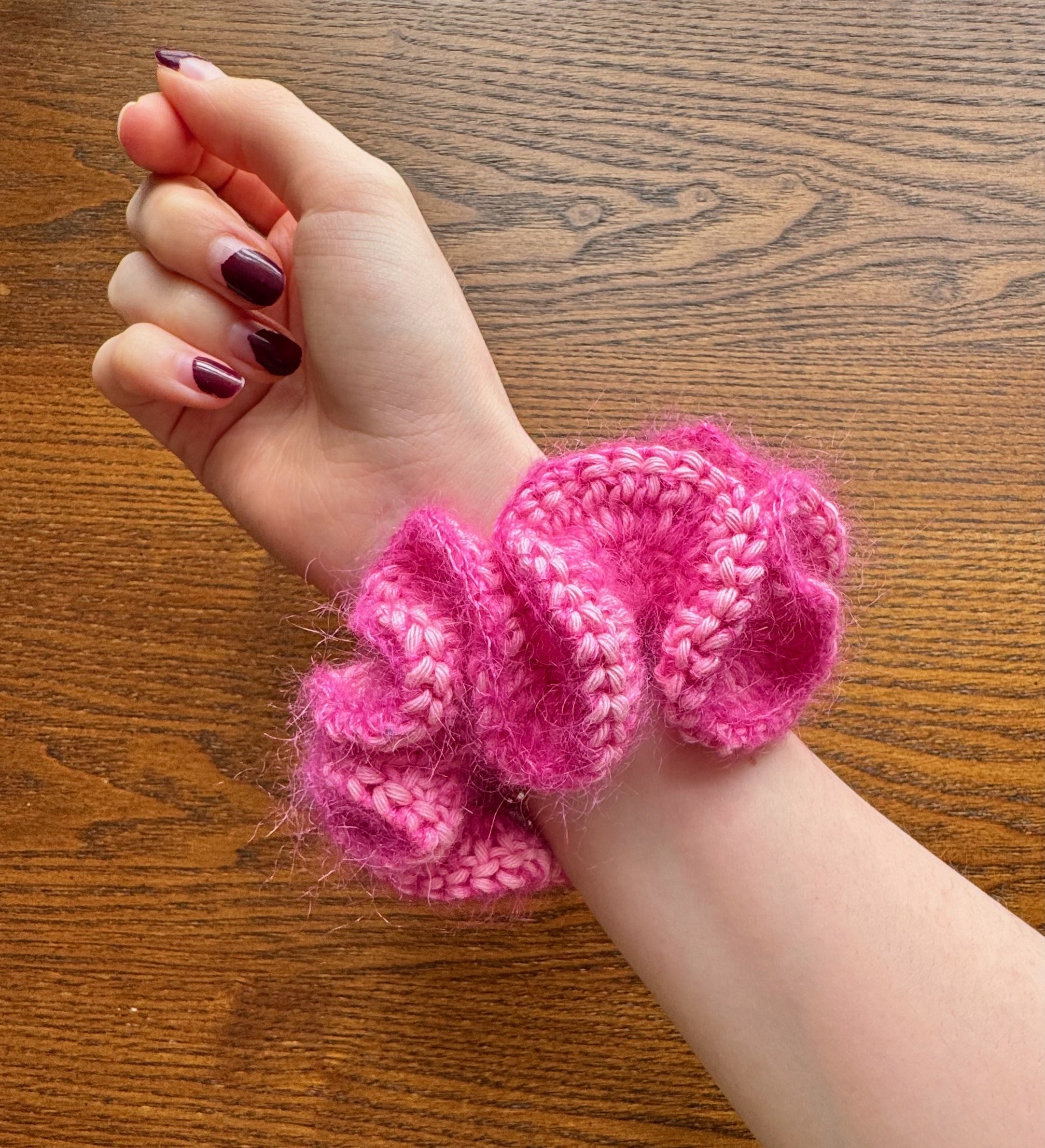 A pink mohair and cotton crochet ruffle scrunchie being worn on a wrist