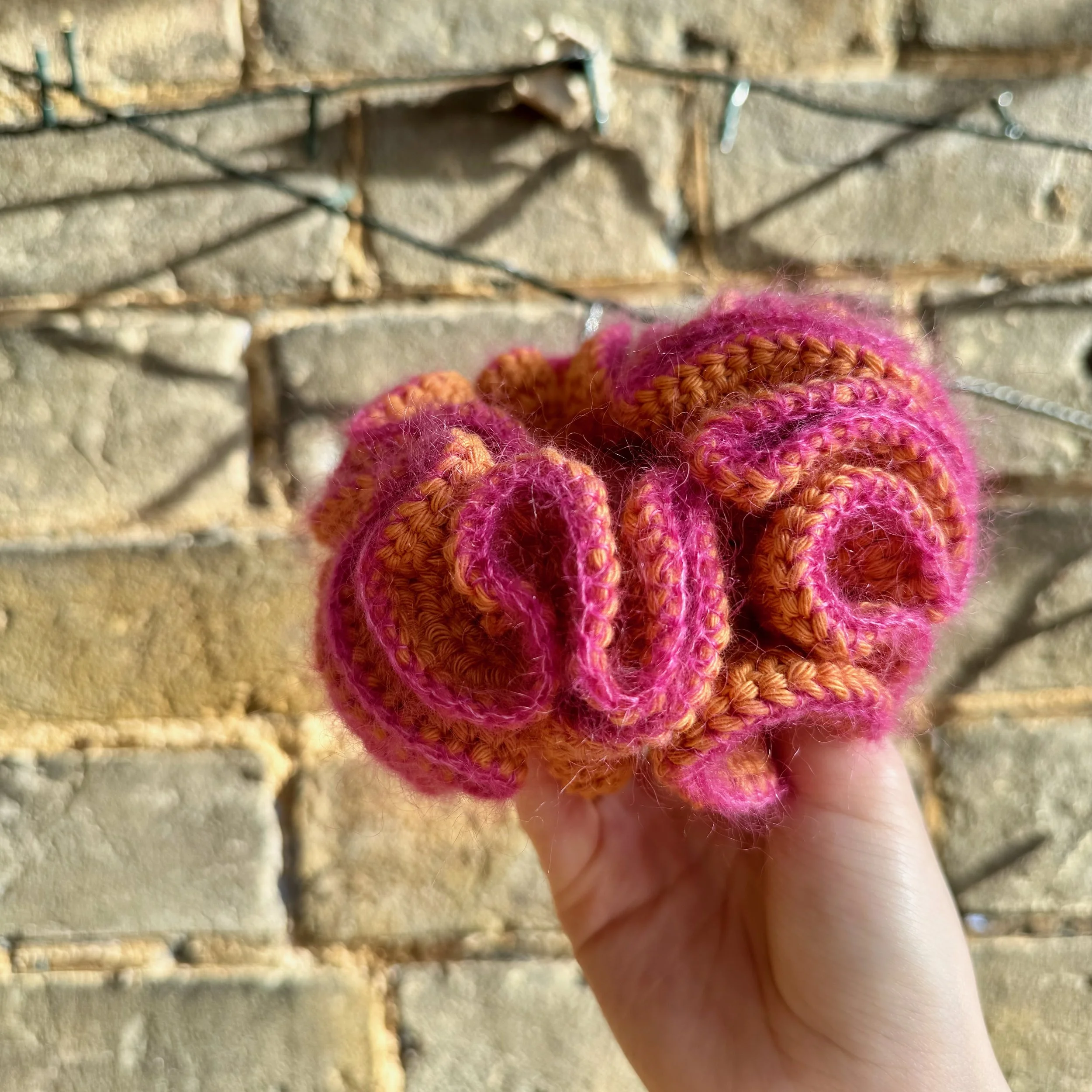 An orange crochet ruffle scrunchie with a pink mohair trim