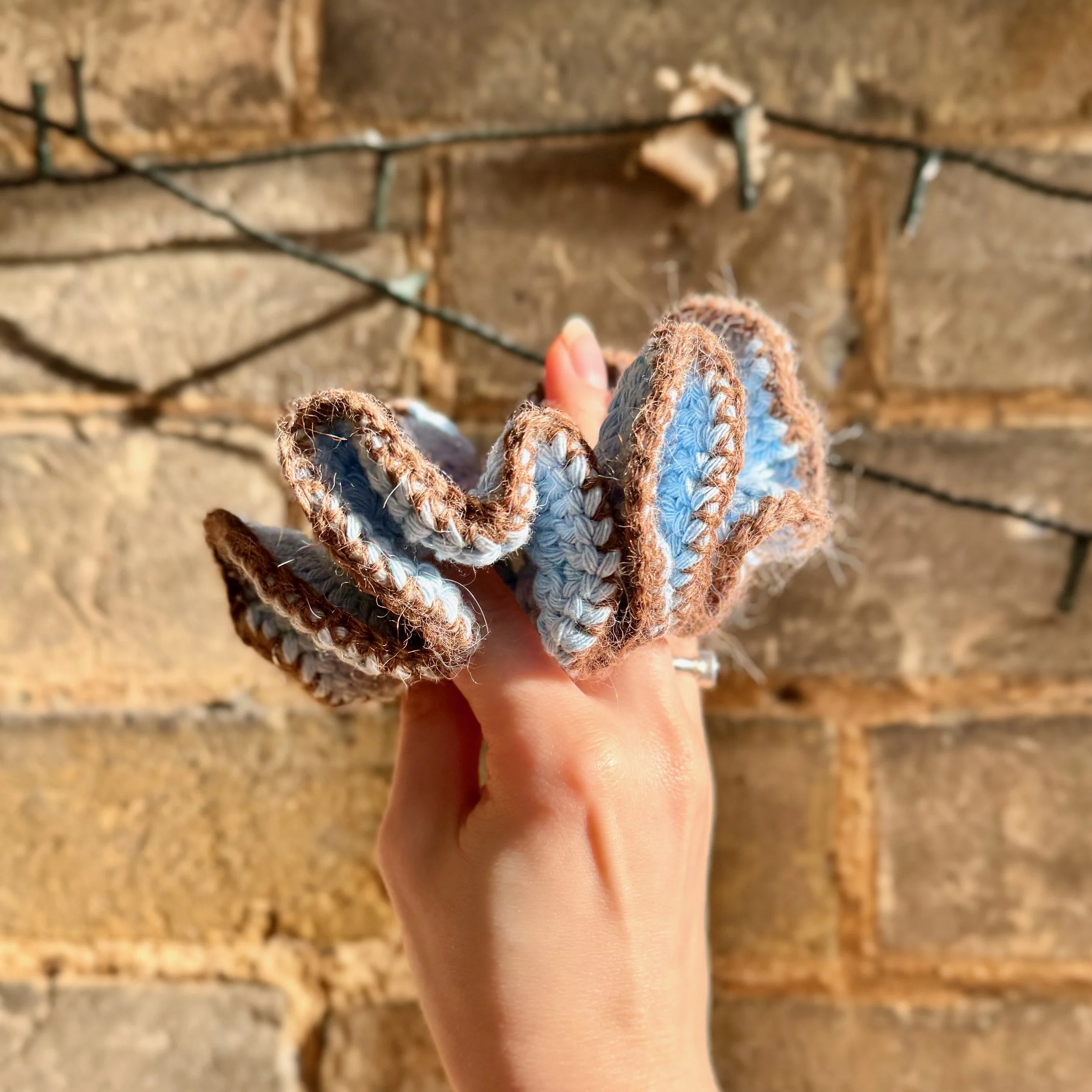 A light blue cotton crochet ruffle scrunchie with a brown alpaca trim being held to show the ruffles