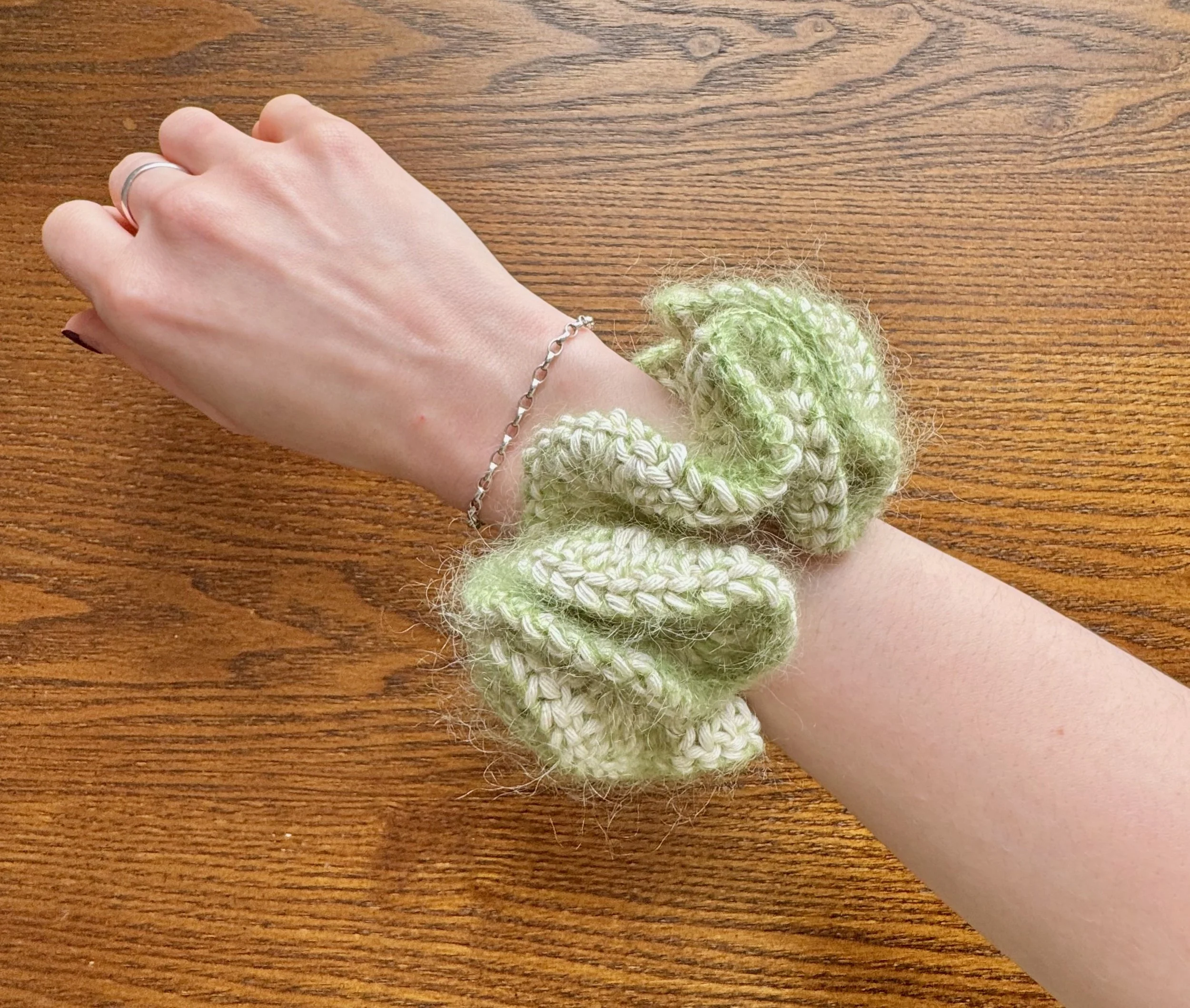 A light green mohair and cotton crochet ruffle scrunchie being worn on a wrist