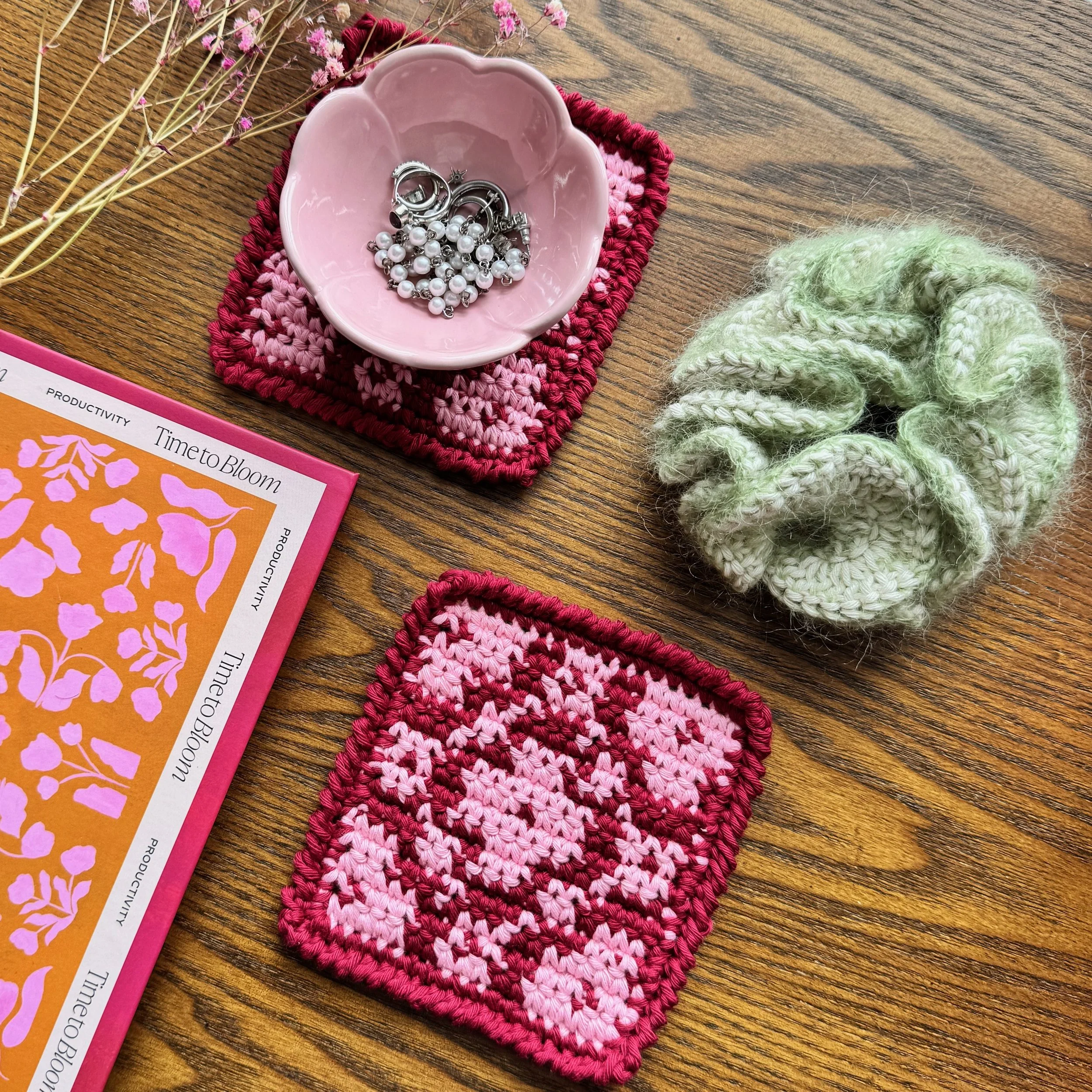A light green mohair and cotton crochet ruffle scrunchie laying flat next to some coasters and a trinket dish.