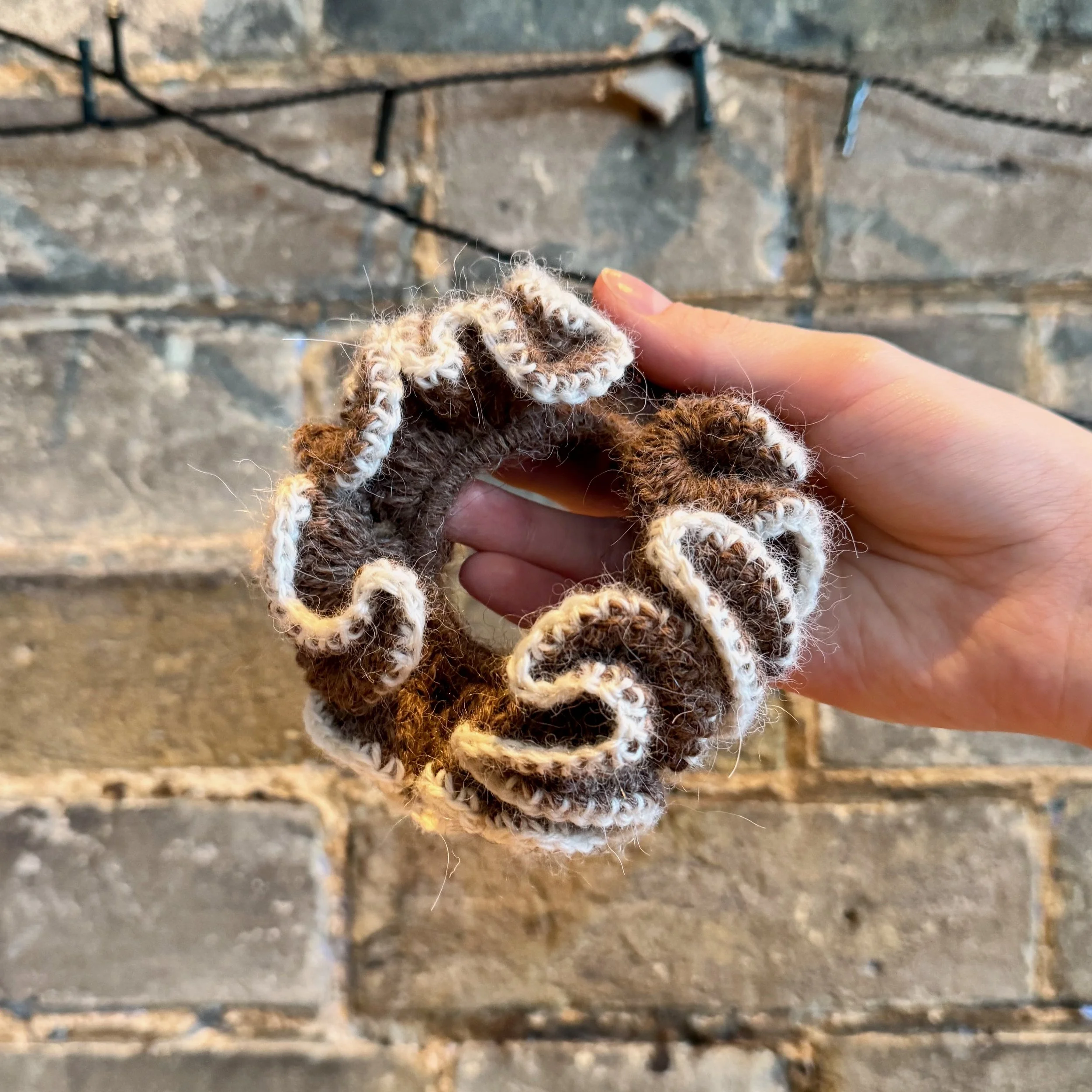 A brown alpaca crochet ruffle scrunchie with a white alpaca trim being held to show the ruffles