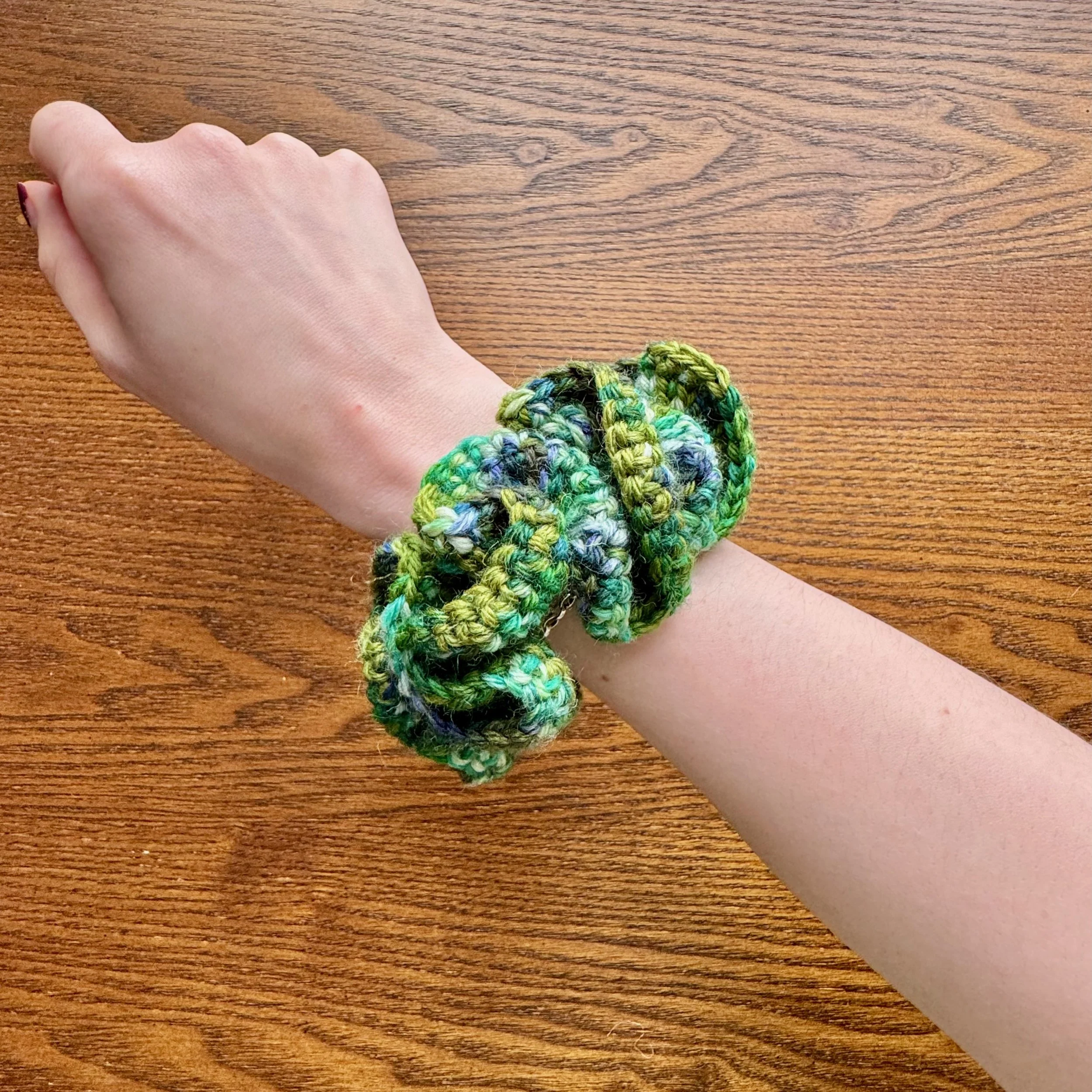 A multi green crochet ruffle scrunchie being worn on a wrist