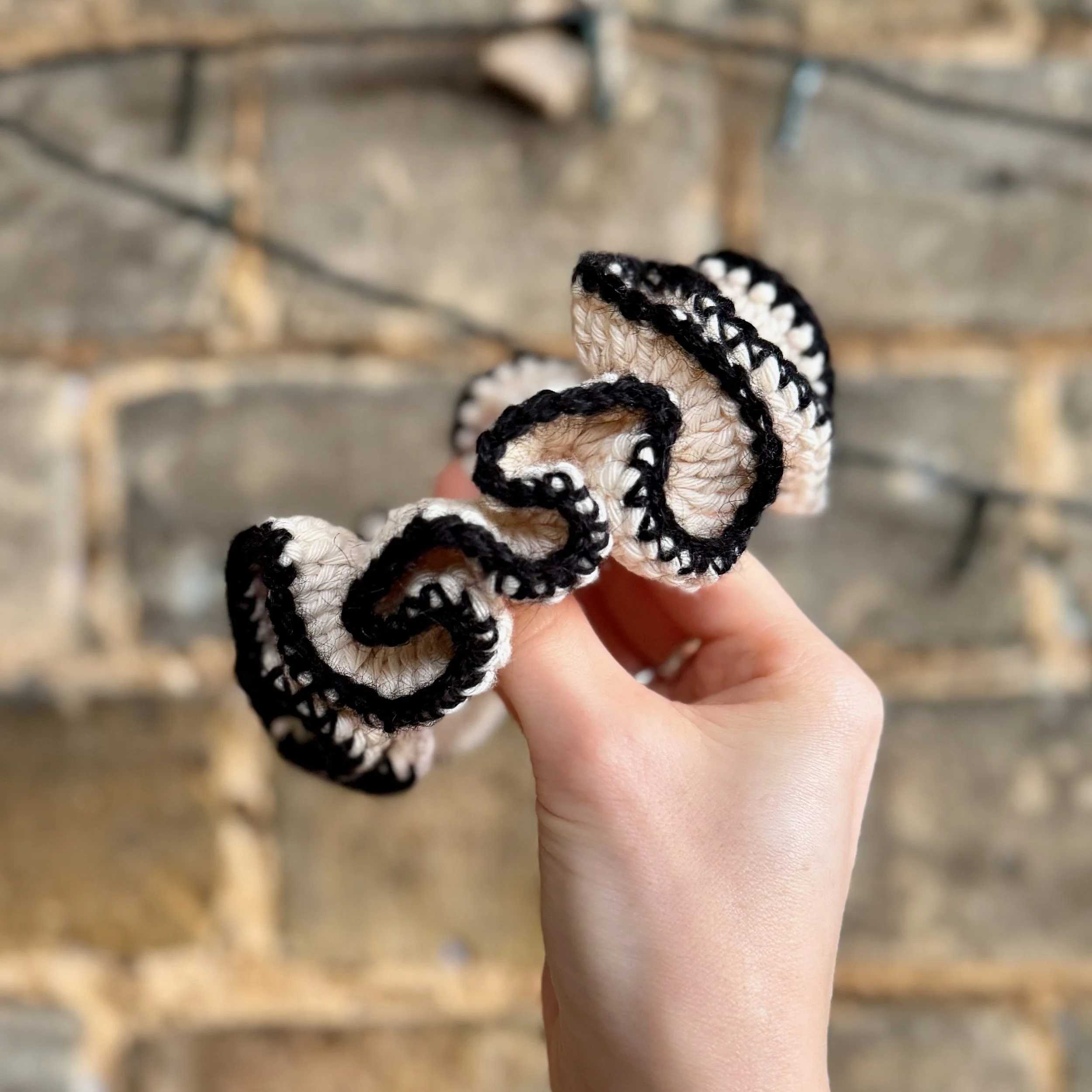 A cream cotton crochet ruffle scrunchie with a black alpaca trim being held to show the ruffles