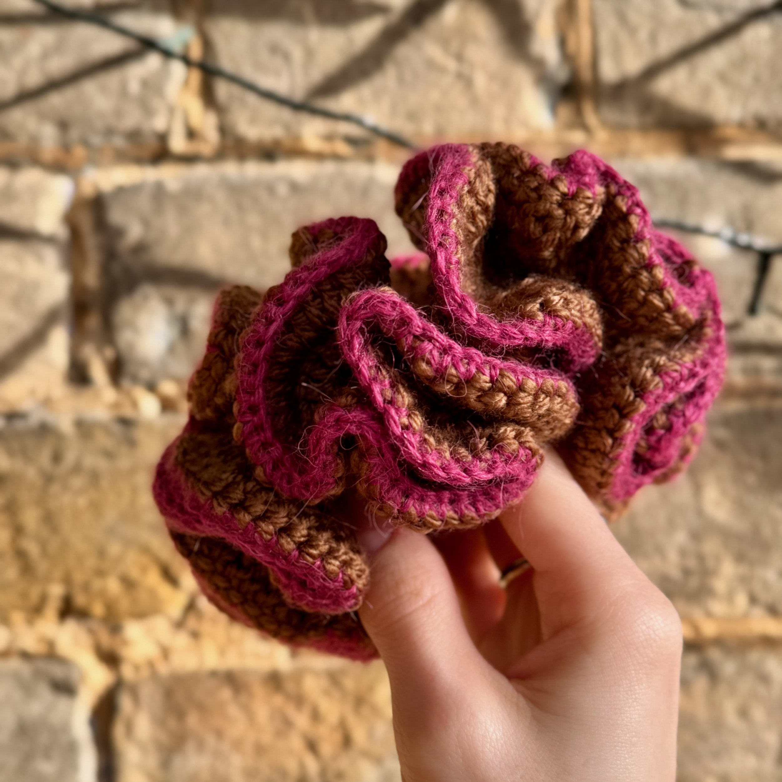 A brown crochet ruffle scrunchie with a pink alpaca trim being held to show the ruffles