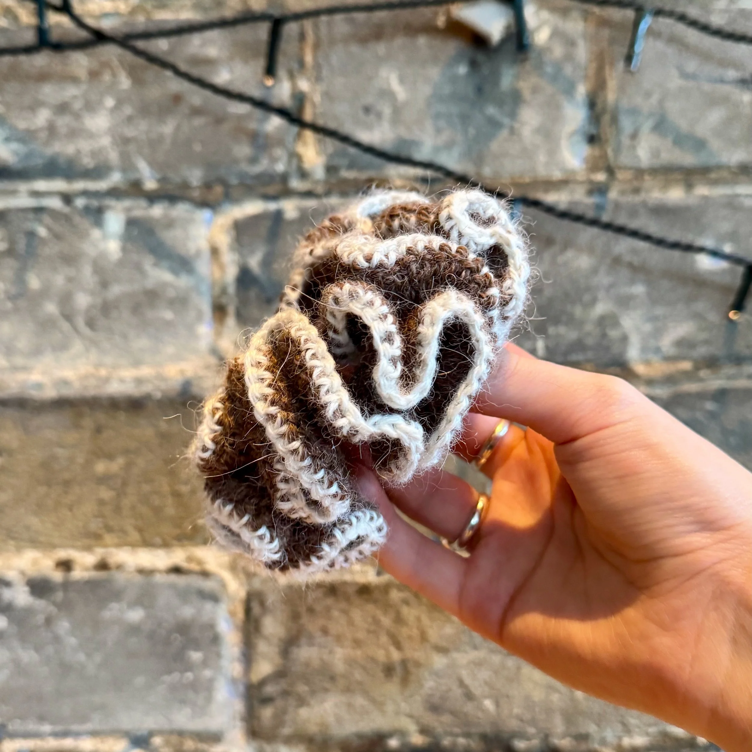 A brown alpaca crochet ruffle scrunchie with a white alpaca trim being held to show the ruffles