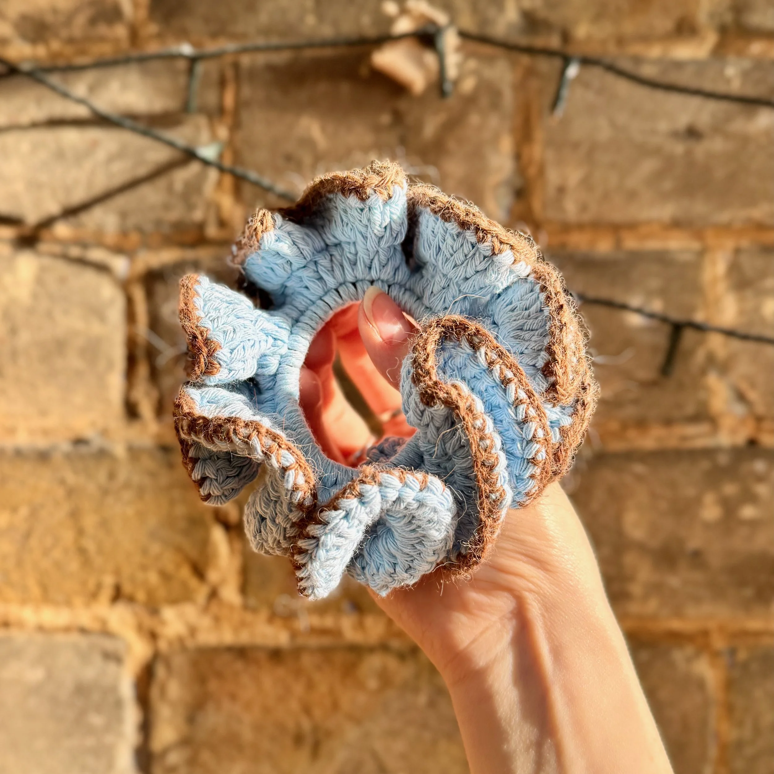 A light blue cotton crochet ruffle scrunchie with a brown alpaca trim being held to show the ruffles