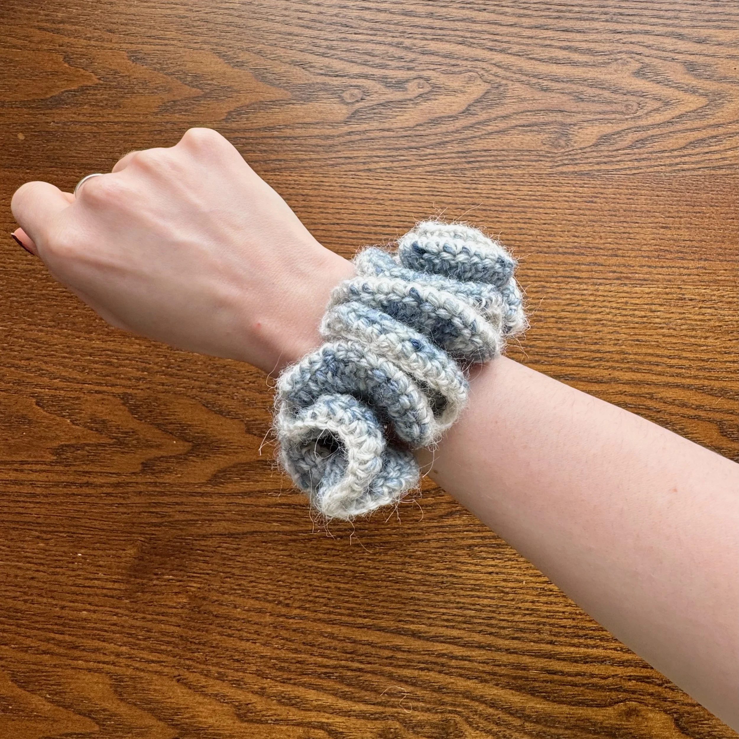 A multi blue woollen crochet ruffle scrunchie that looks like denim with a white alpaca trim being worn on a wrist