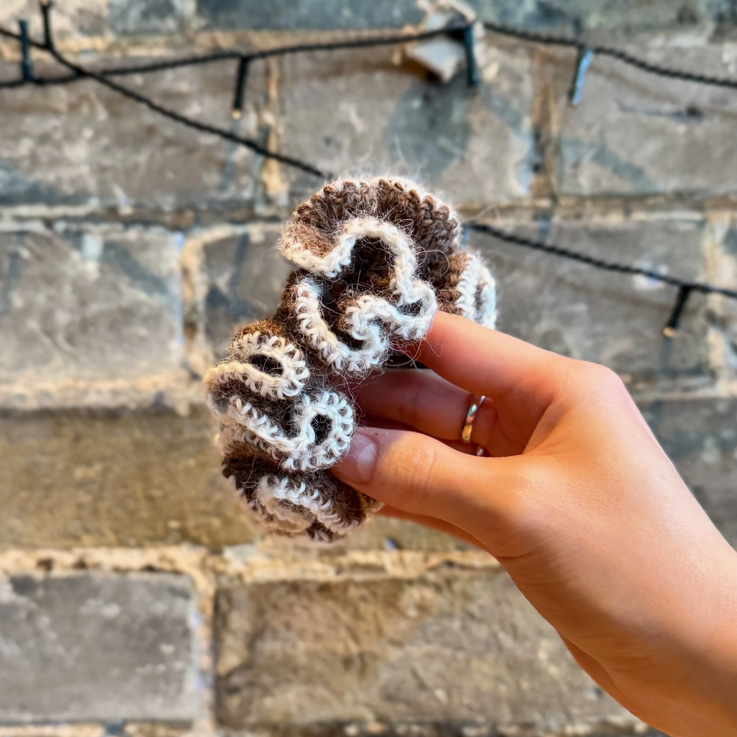A brown alpaca crochet ruffle scrunchie with a white alpaca trim being held to show the ruffles
