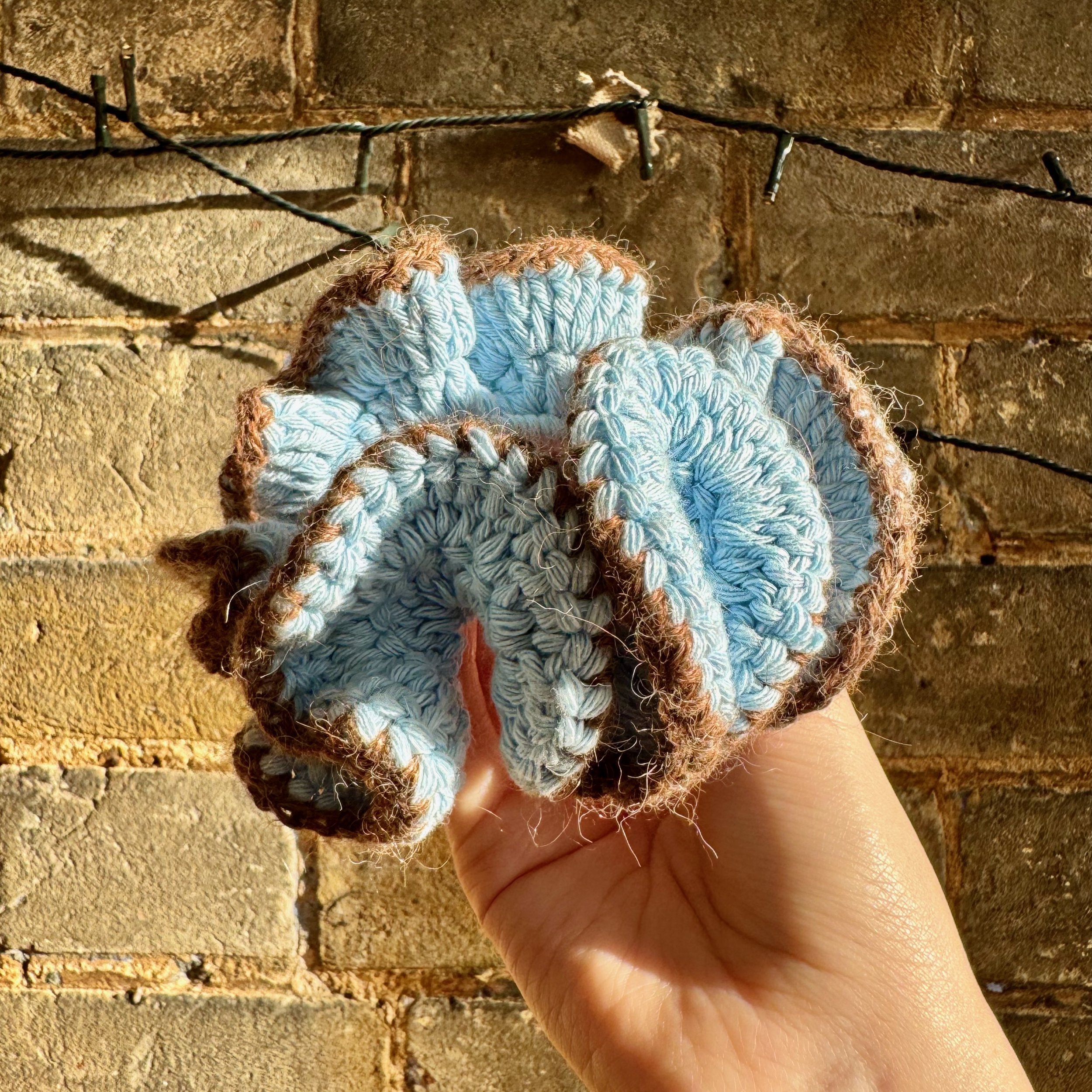 A light blue cotton crochet ruffle scrunchie with a brown alpaca trim being held to show the ruffles