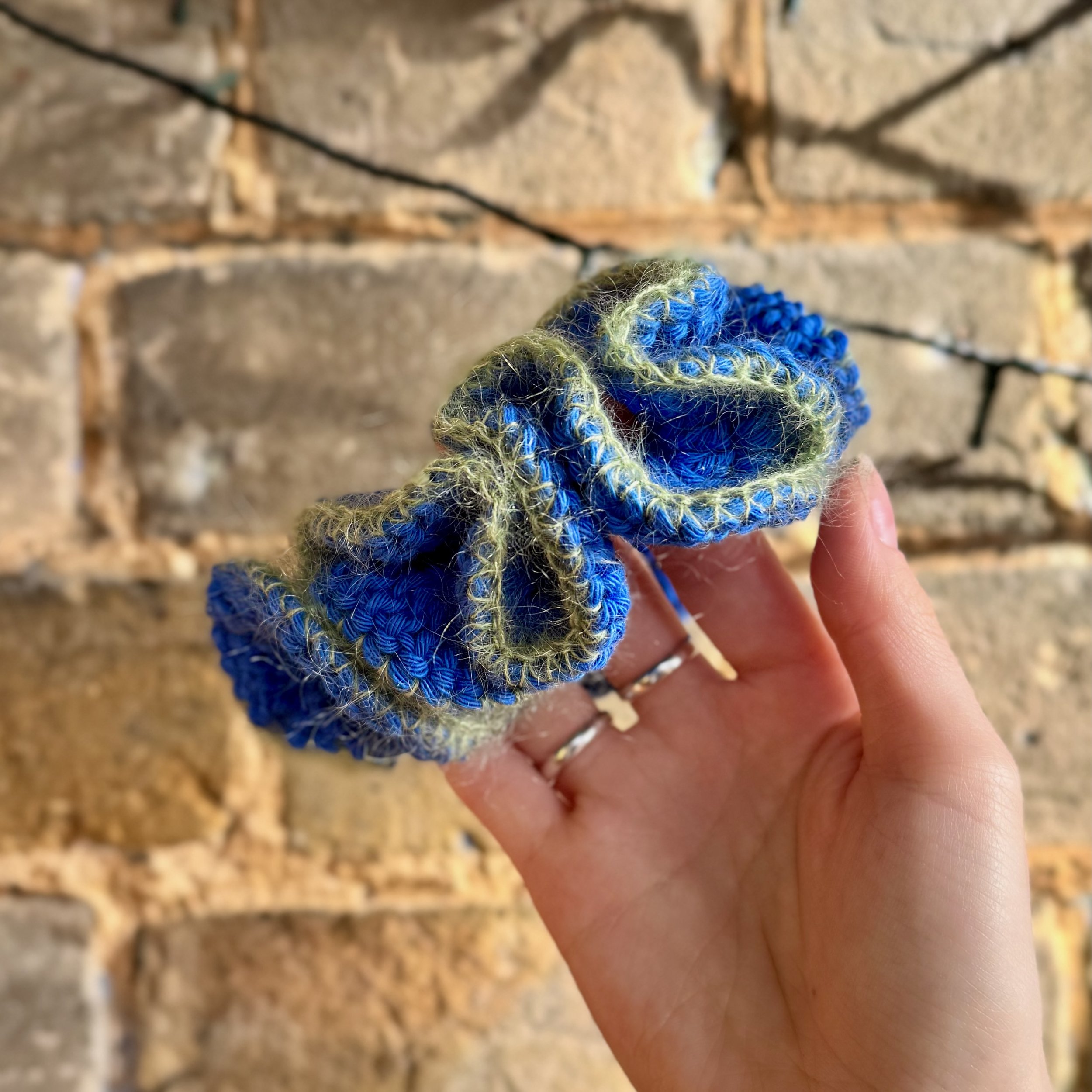 A bright blue cotton crochet ruffle scrunchie with a green mohair trim being held to show the ruffles