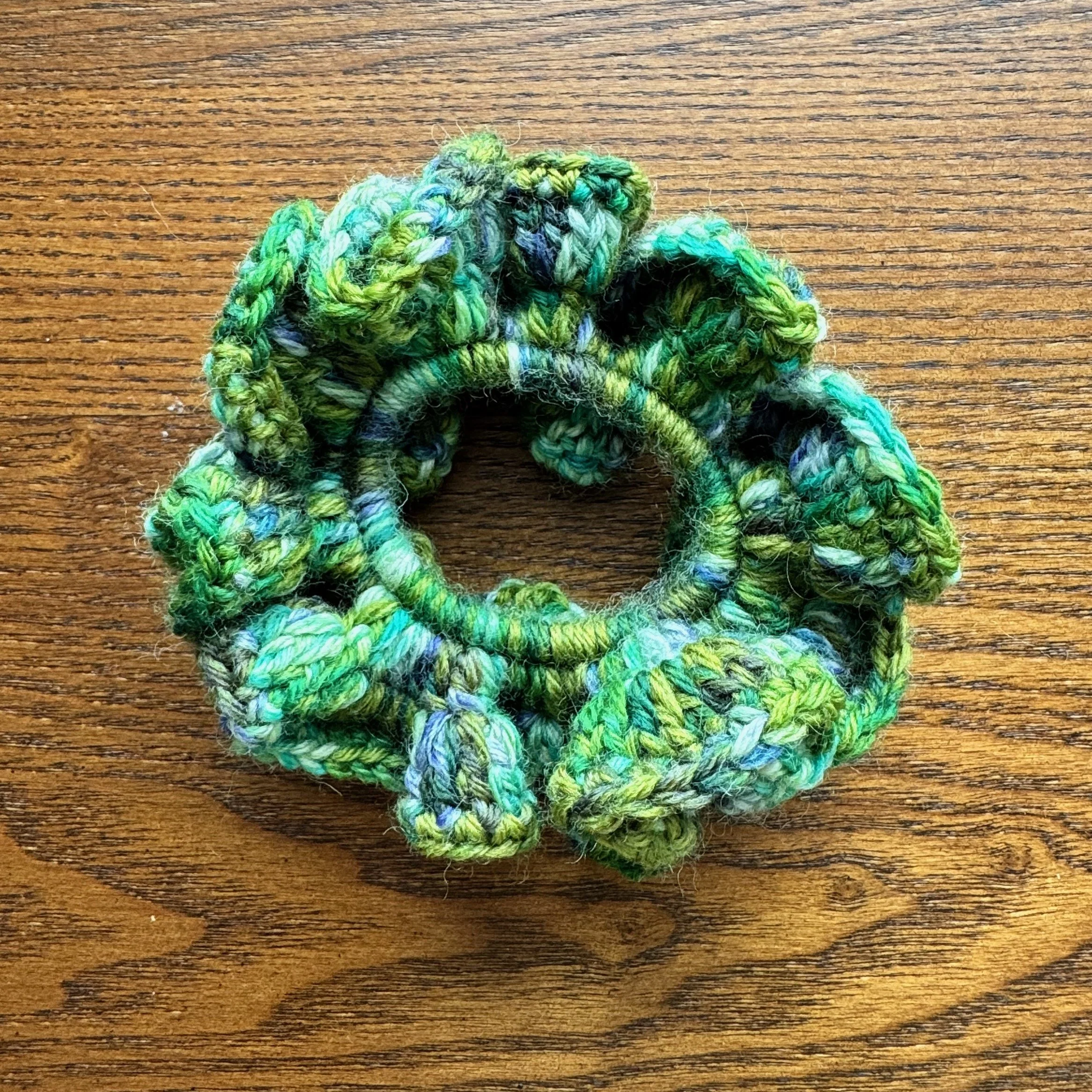 A multi green crochet ruffle scrunchie laying flat on a surface