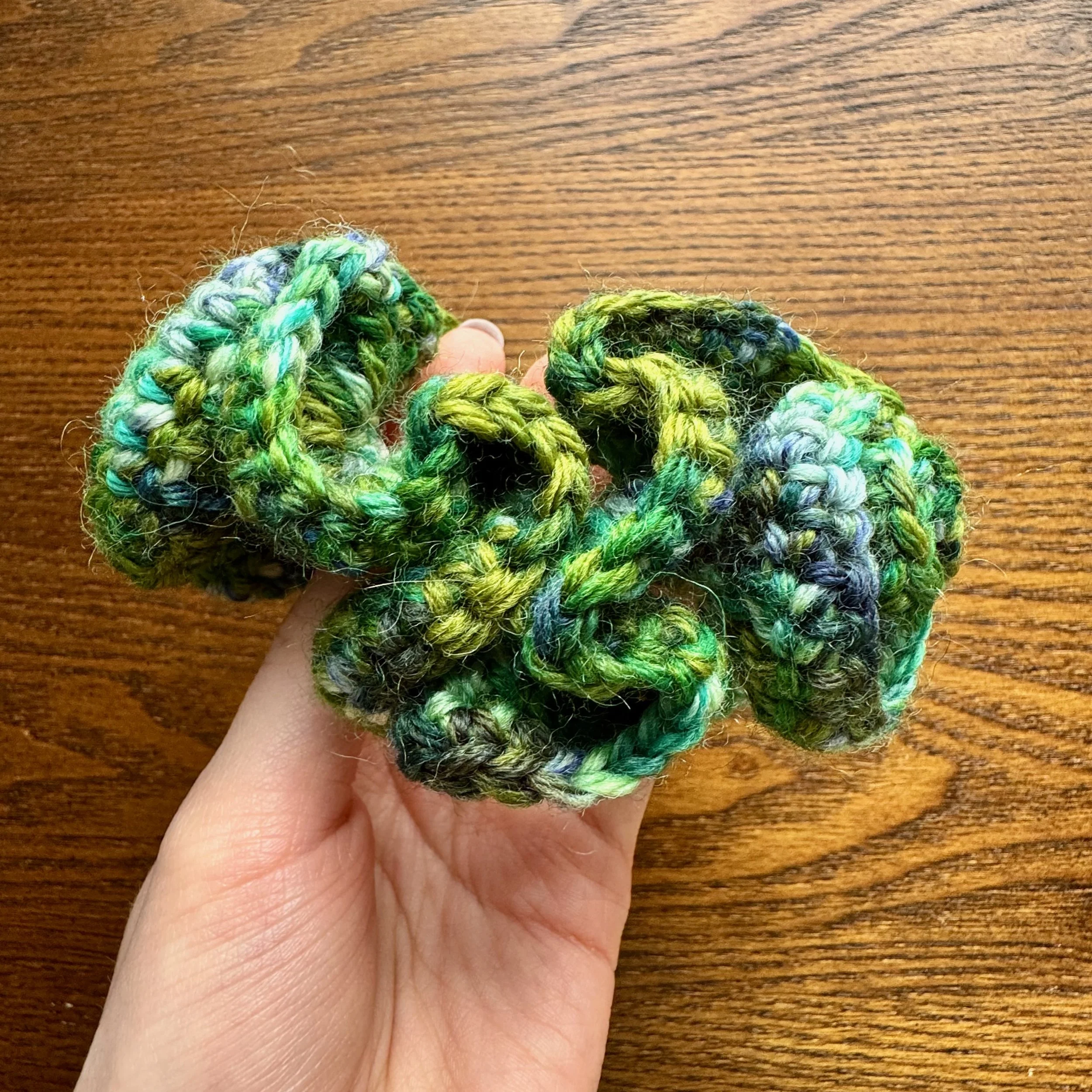 A multi green crochet ruffle scrunchie being held to show the shape