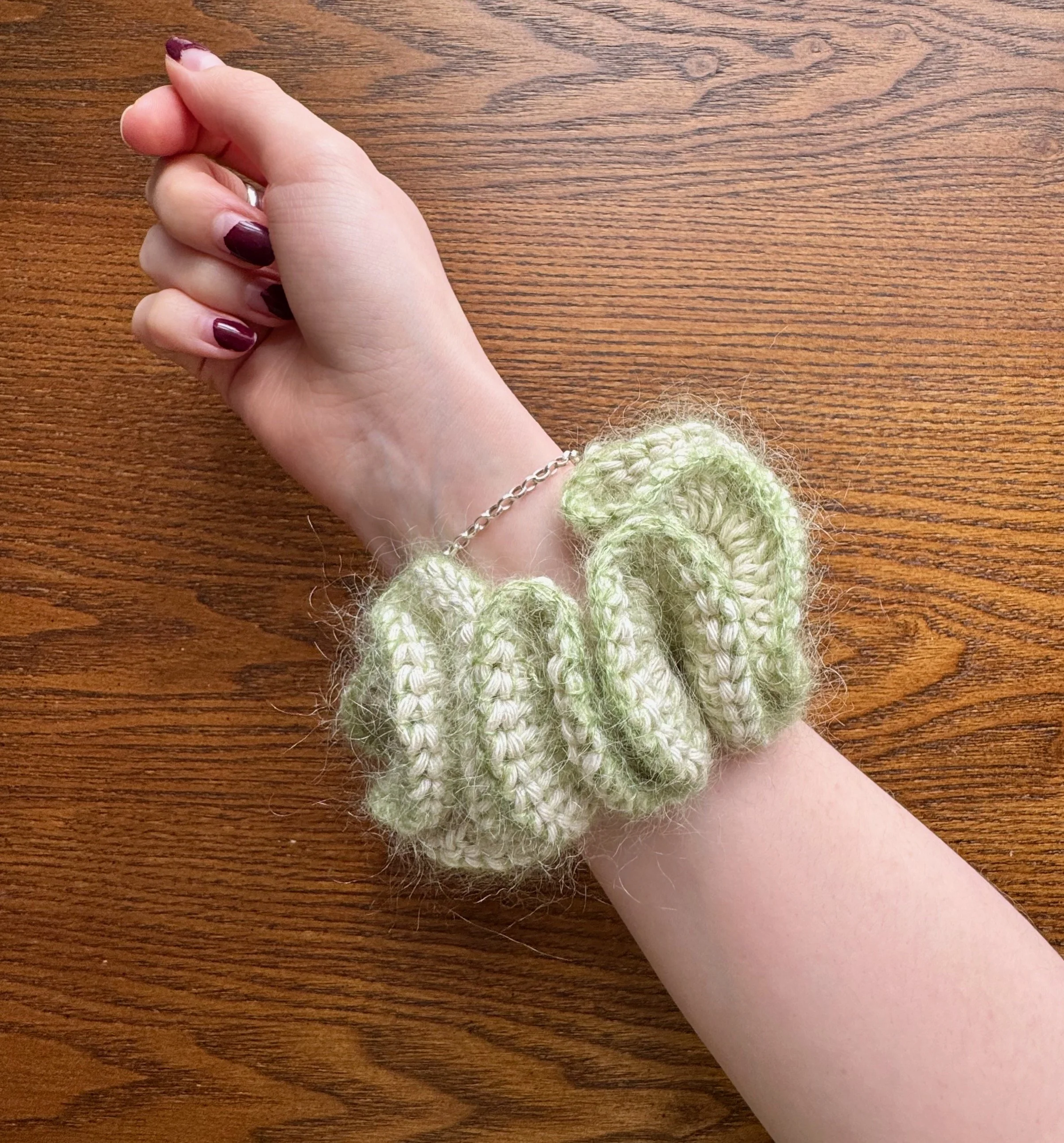 A light green mohair crochet ruffle scrunchie being worn on a wrist