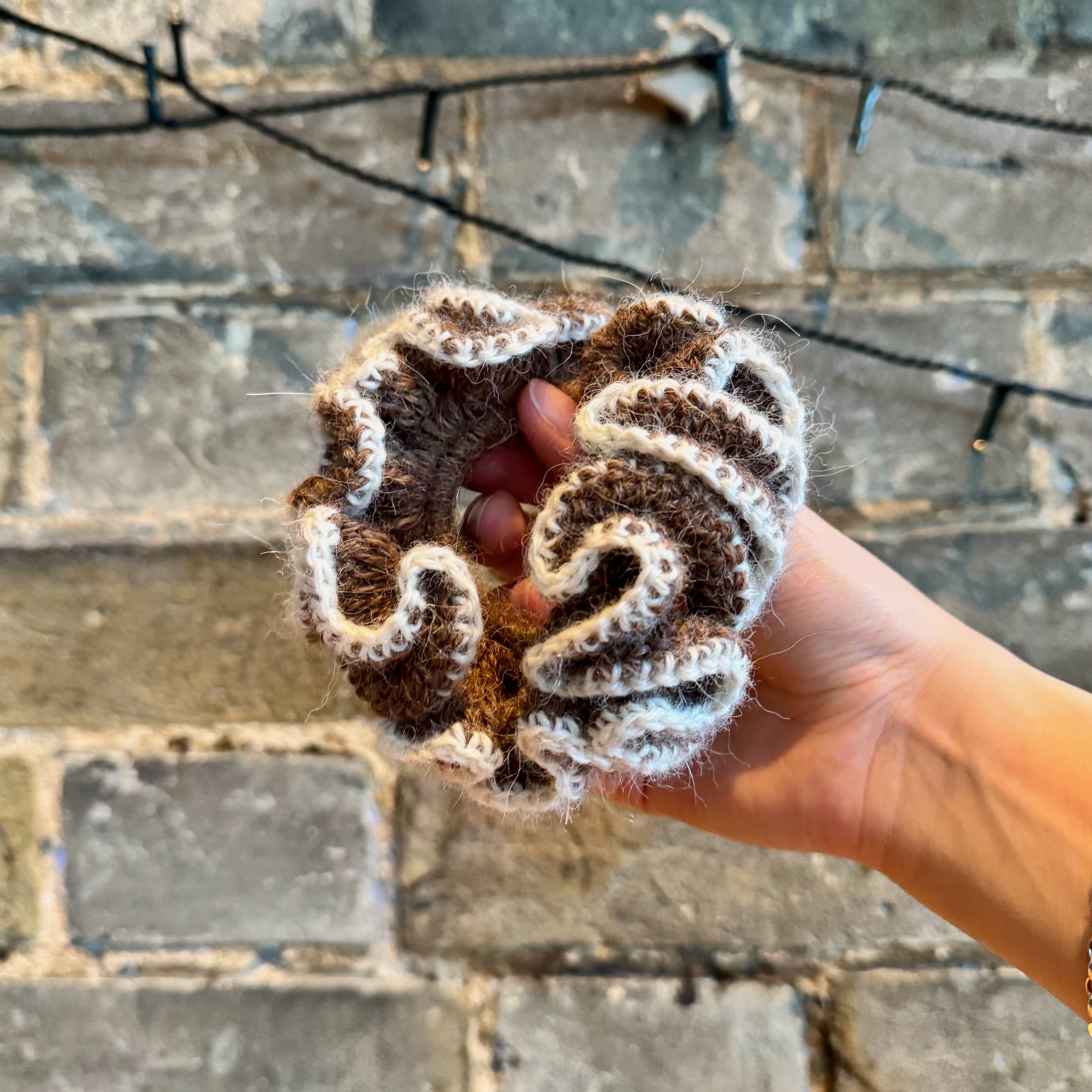 A brown alpaca crochet ruffle scrunchie with a white alpaca trim being held to show the ruffles