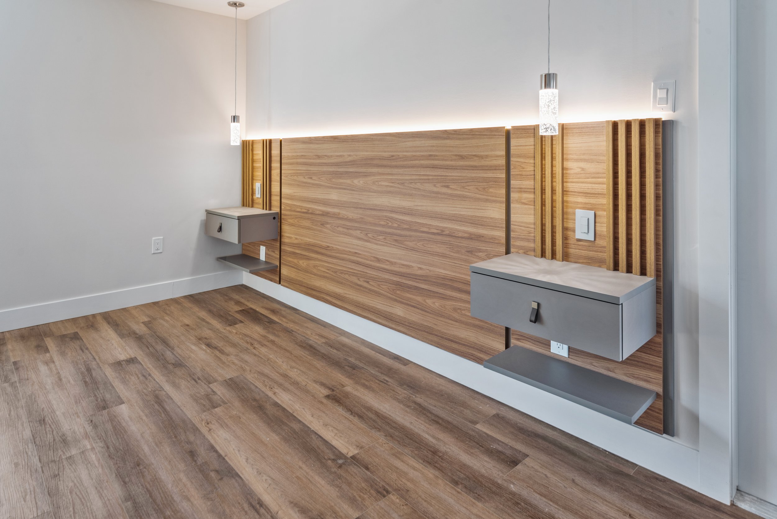 Modern bedroom with wooden wall paneling, floating gray nightstands, and pendant lights.