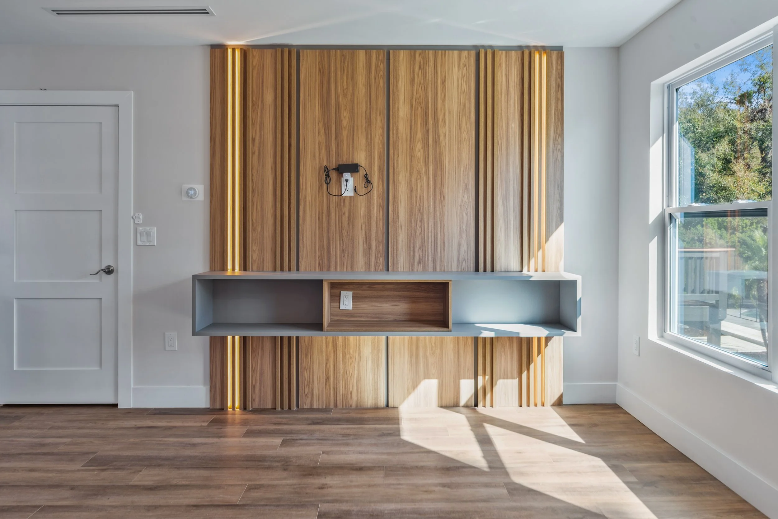 Empty room with wooden accent wall, built-in shelf, and large window with a view of trees outside