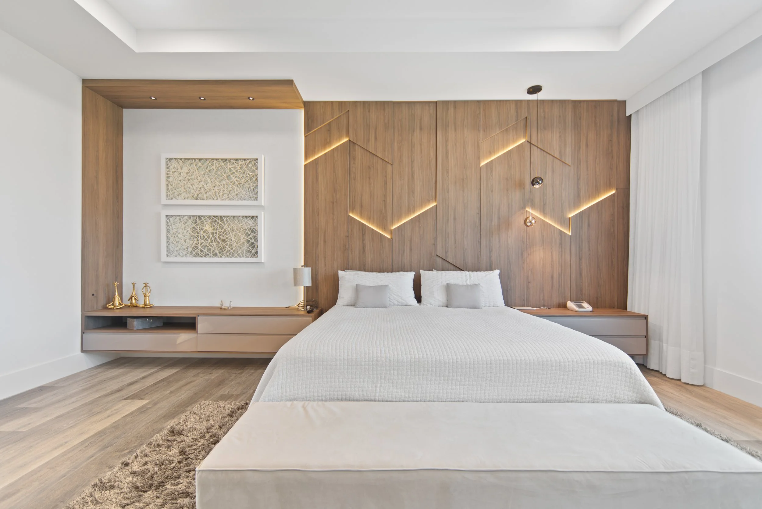 Modern bedroom with white bedding, wooden accent wall with geometric lighting, white curtains, and minimal decor.