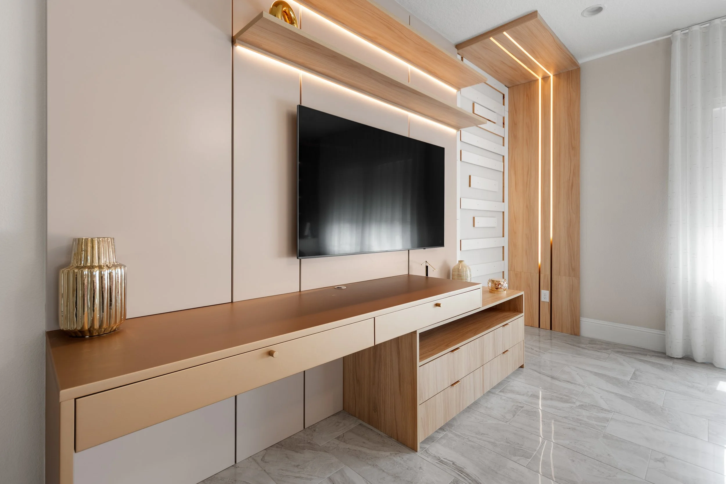 Modern living room entertainment area with a mounted flat-screen TV on a beige wall, a wooden TV console with drawers, decorative vases, and a wood-paneled wall feature with LED lighting, all on a light-colored tile floor.
