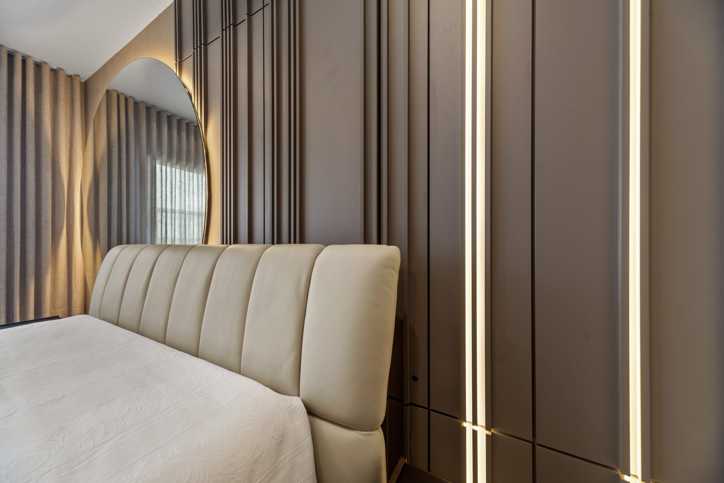 Modern bedroom with beige upholstered bed, large mirror, and wooden panel wall with integrated vertical lighting accents.