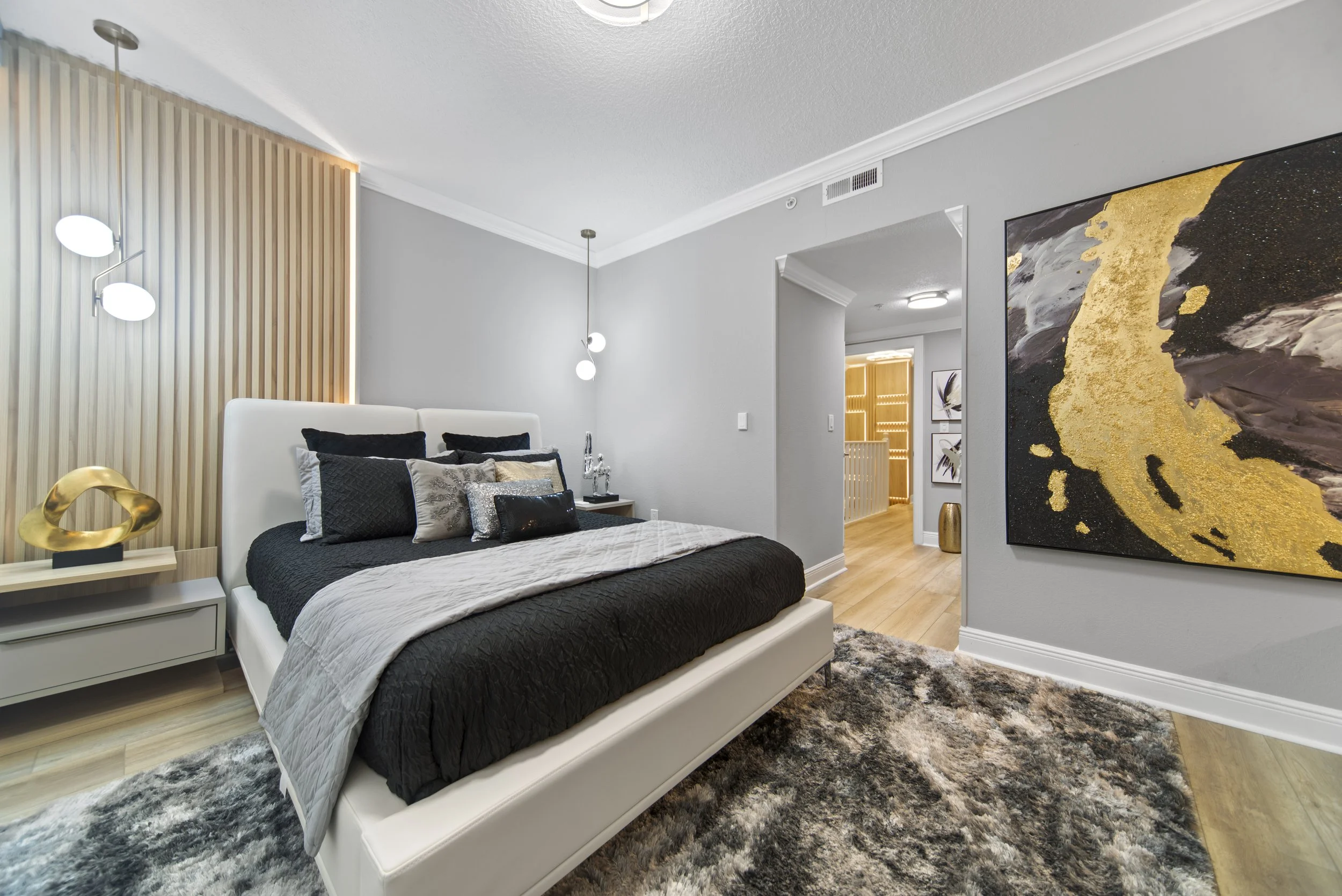 Modern bedroom with a black bedspread, multiple pillows, wooden flooring, contemporary wall art, and decorative lighting.