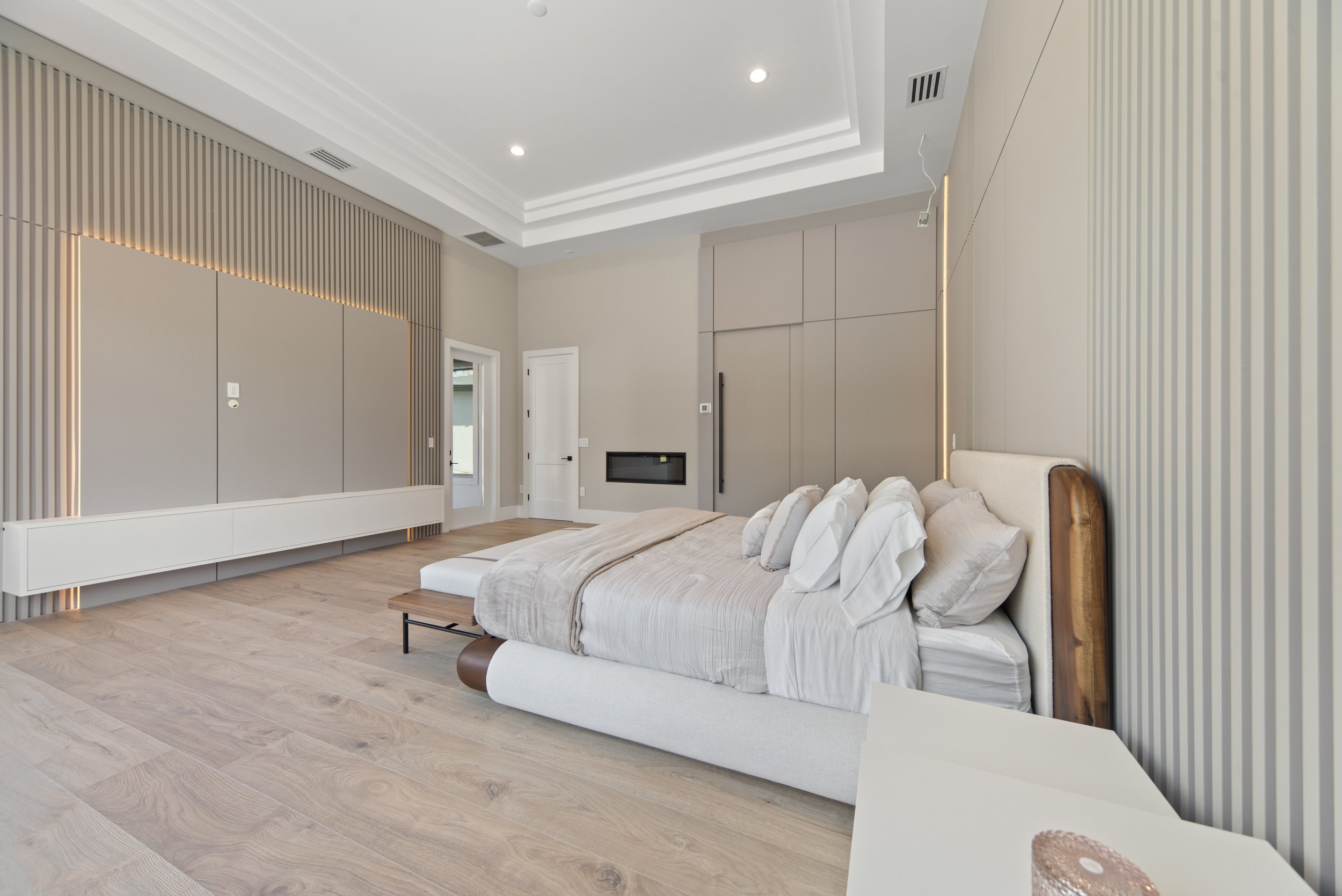 Modern bedroom with a king-sized bed, beige and white bedding, and neutral-colored walls and flooring.