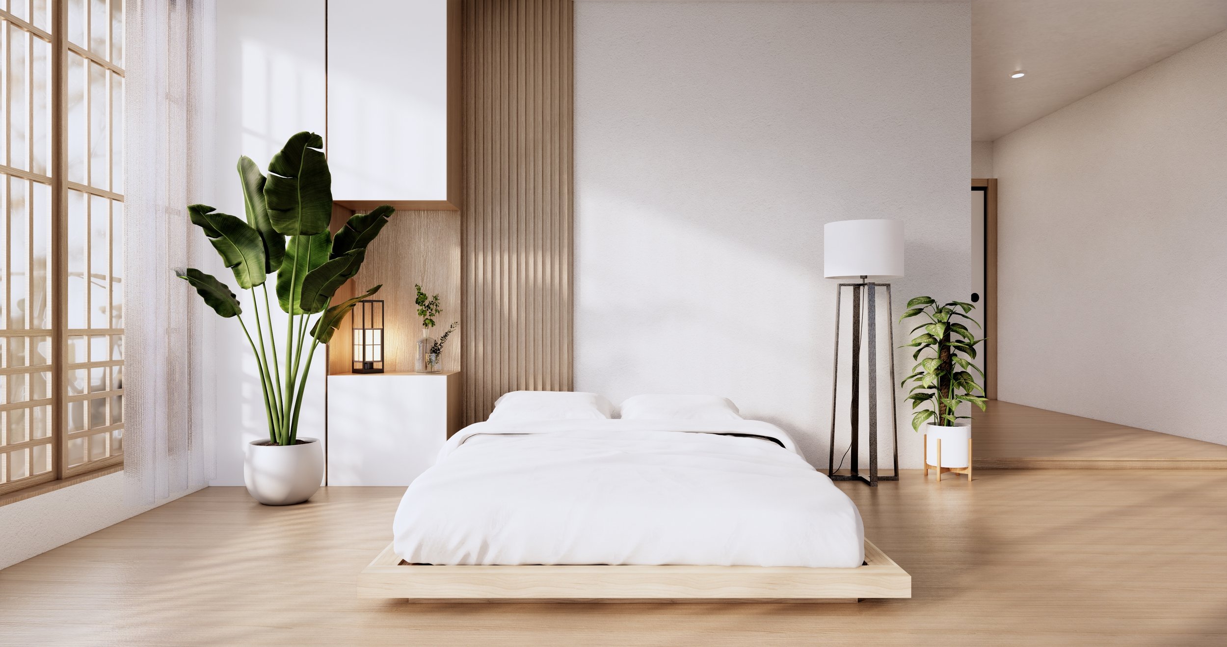 Minimalist bedroom with a low white bed, potted plants, a wooden floor, and a soft natural light coming through a shoji screen.