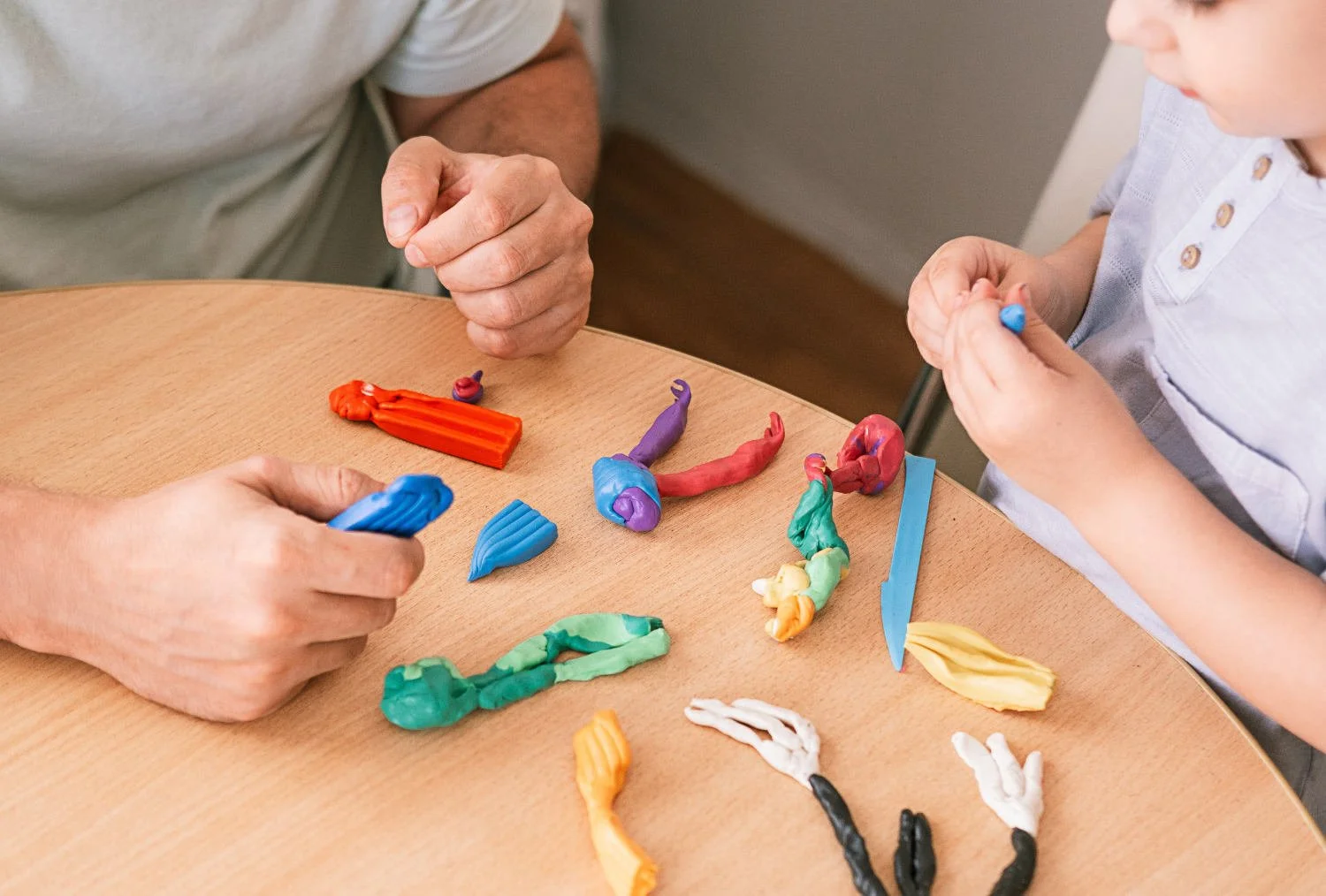 Children and an adult playing with colorful modeling clay on a wooden table.