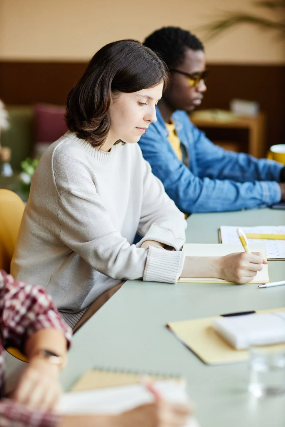 Young woman taking notes during a meeting with others at a conference table.
