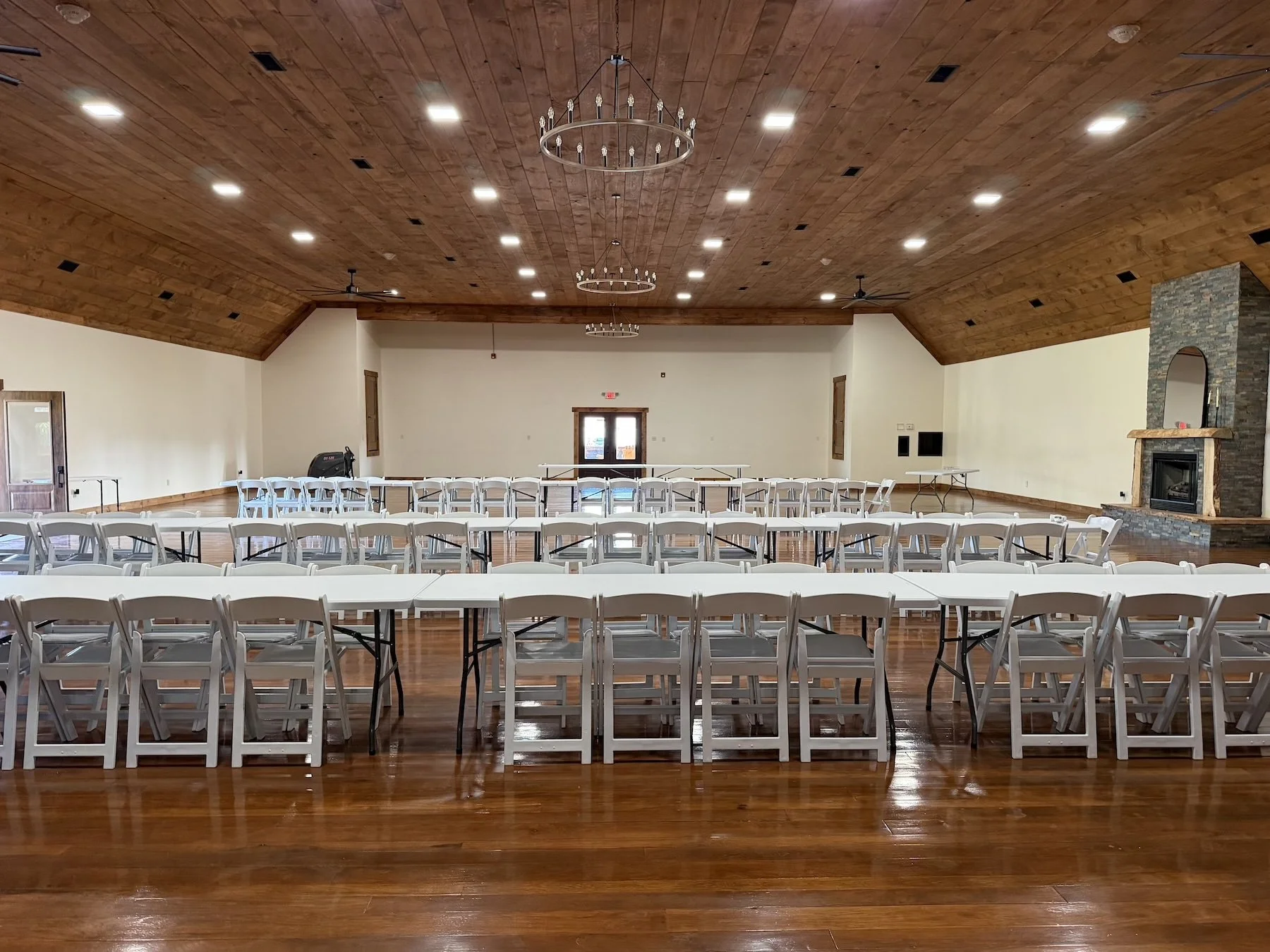 Spacious reception hall at God's Country Venue in Oak Hill, Ohio, featuring wood ceilings, chandeliers, polished floors, tables, and white chairs.