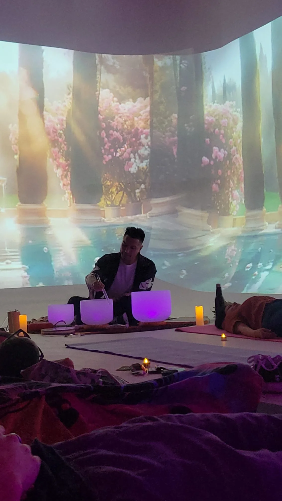 Alex Ma playing the Crystal singing bowls at a Solar Soul Circle sound healing event. the bowls are lit purple with candles to light the path for guests attending.