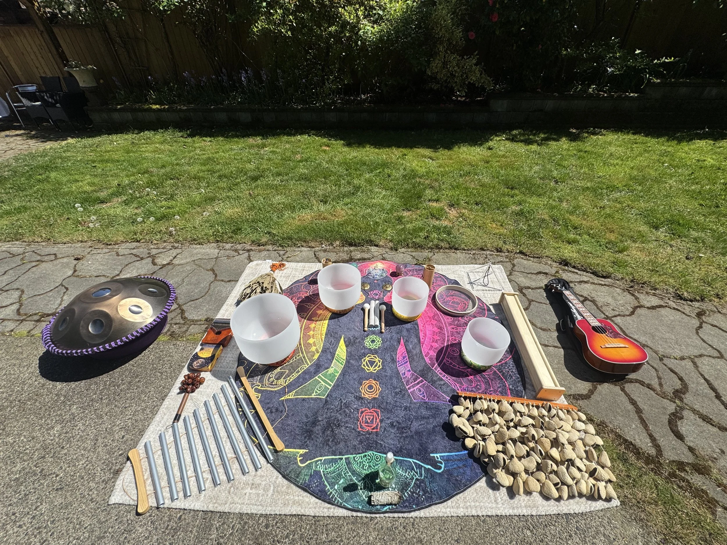 A mat with an image of the 7 chakras and sound healing instruments laid out on them for a birthday party in North Vancouver including crystal singing bowls, Chakapa, chimes, handpan, ukulele, rain stick, ocean drum and kalimba.