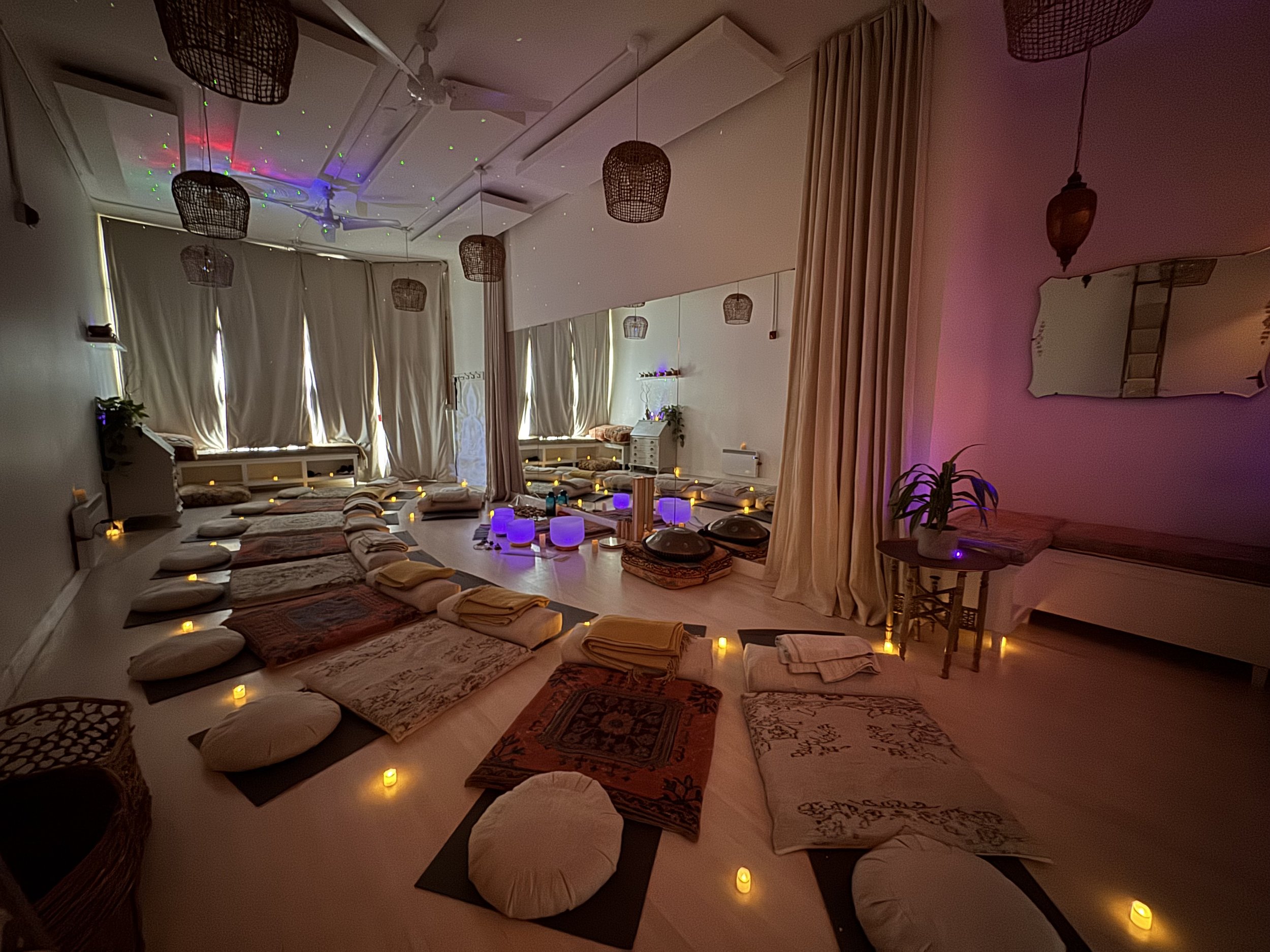 Sound therapy relaxation space in Vancouver with yoga mats, blankets, pillows, glowing crystal singing bowls, candles, and soft ambient lighting.