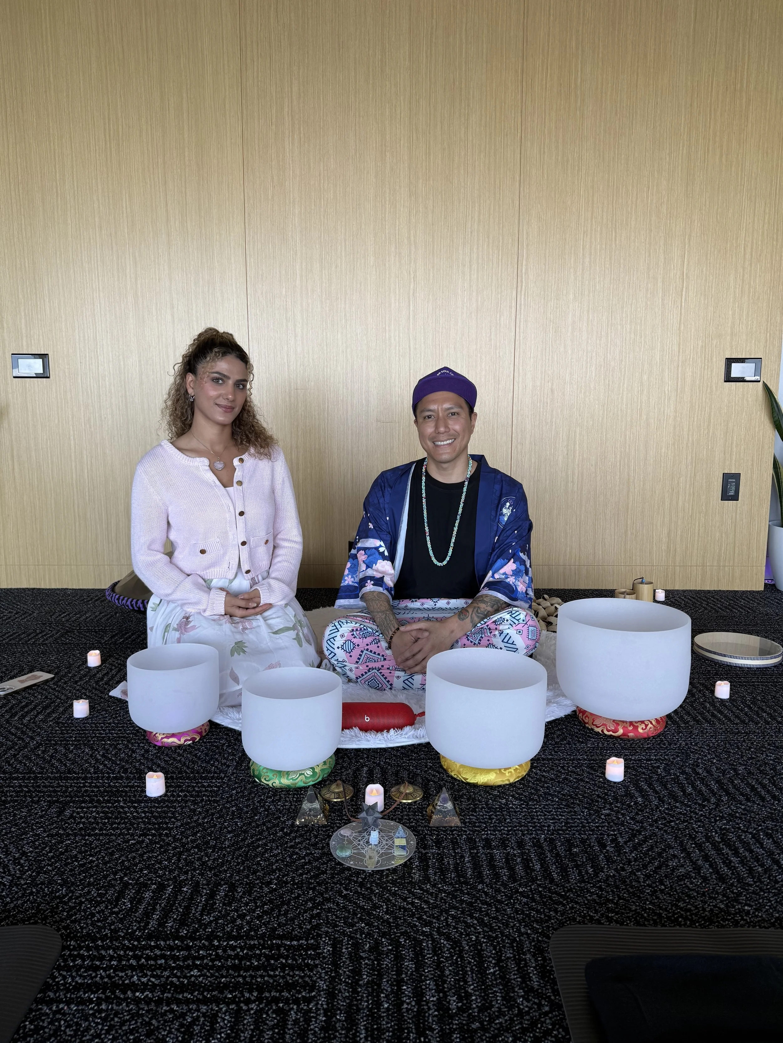 Alex Ma and Saja Light from Solar Soul Circle smiling, sitting around crystal singing bowls, gems laid out in sacred geometry, orgone pyramids and electronic candles