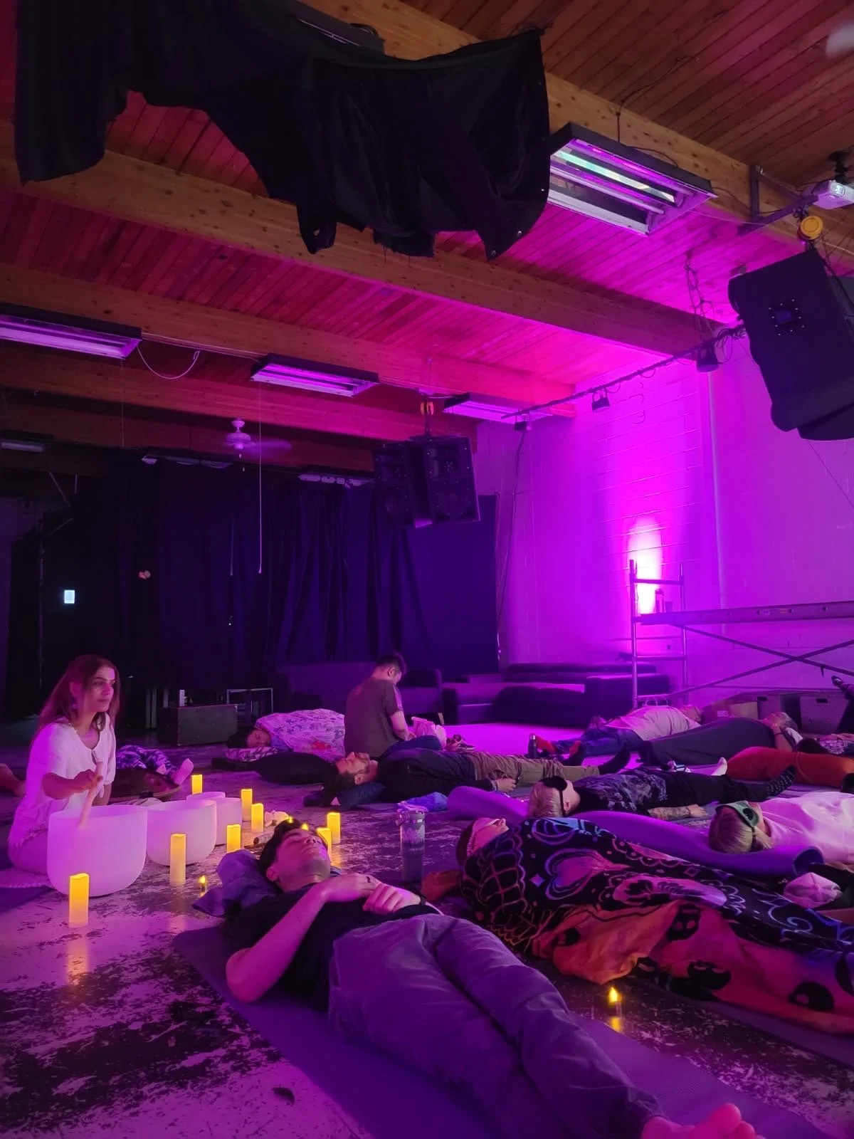 Saja Light playing the sound bowls during a Solar Soul Circle sound bath event with guests meditating in Gastown, Vancouver, BC. With ambient purple lights and candles throughout the room.