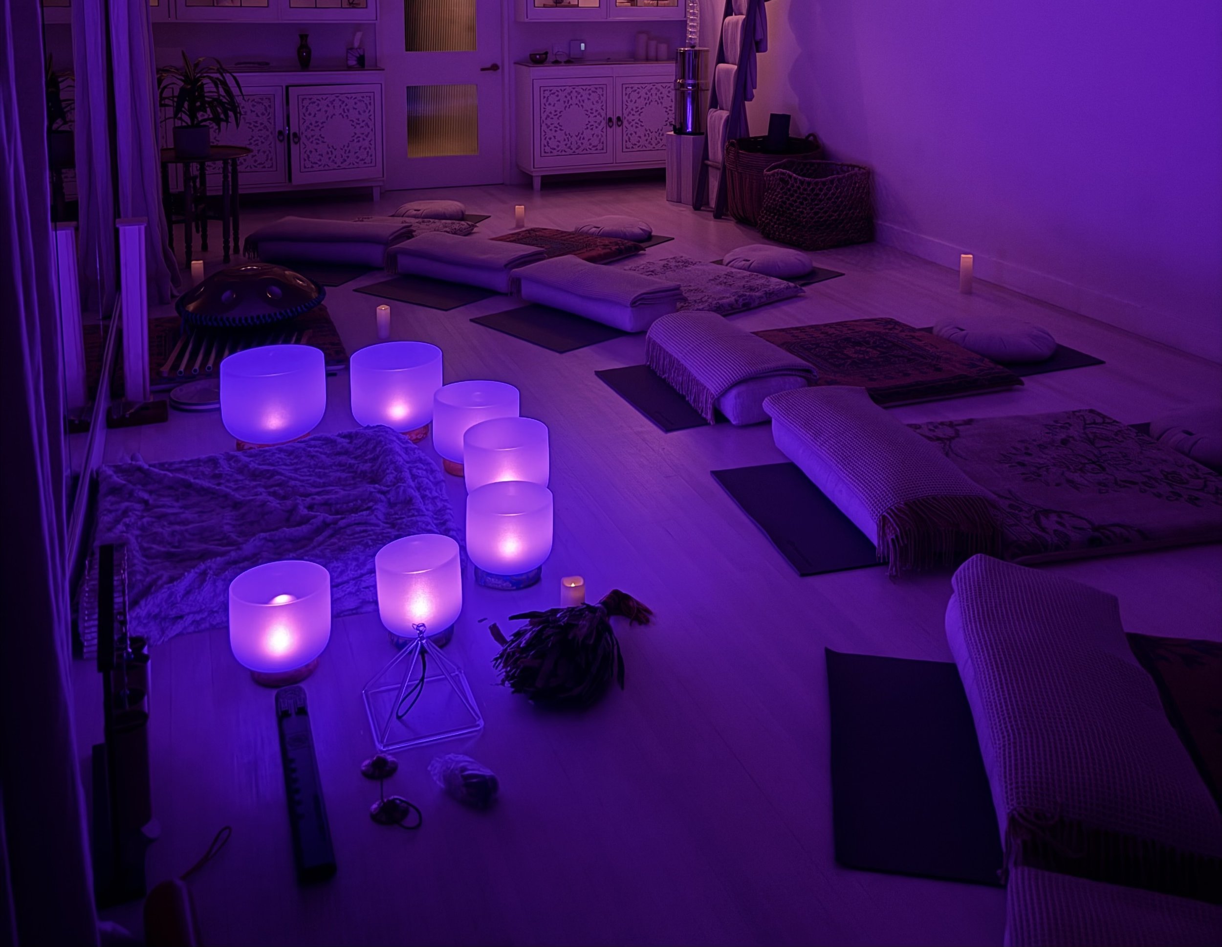Birthday sound bath relaxation space in Vancouver with yoga mats, blankets, pillows, glowing crystal singing bowls, candles, and soft purple lighting.
