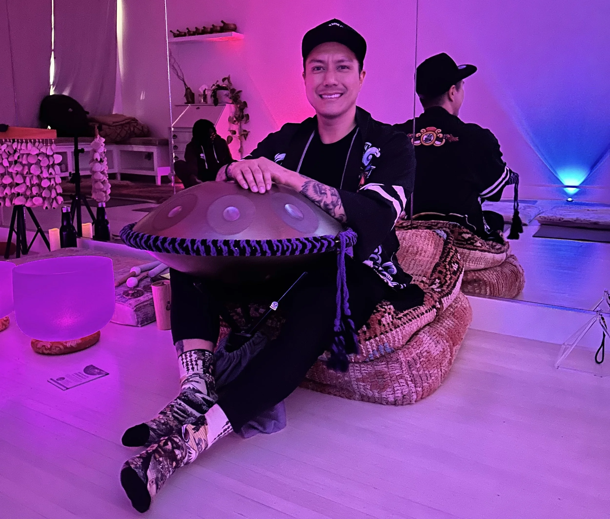 Solar Soul Circle sound bath facilitator holding a handpan in a calming Vancouver studio with crystal singing bowls, chimes, candles, and soft purple lighting.
