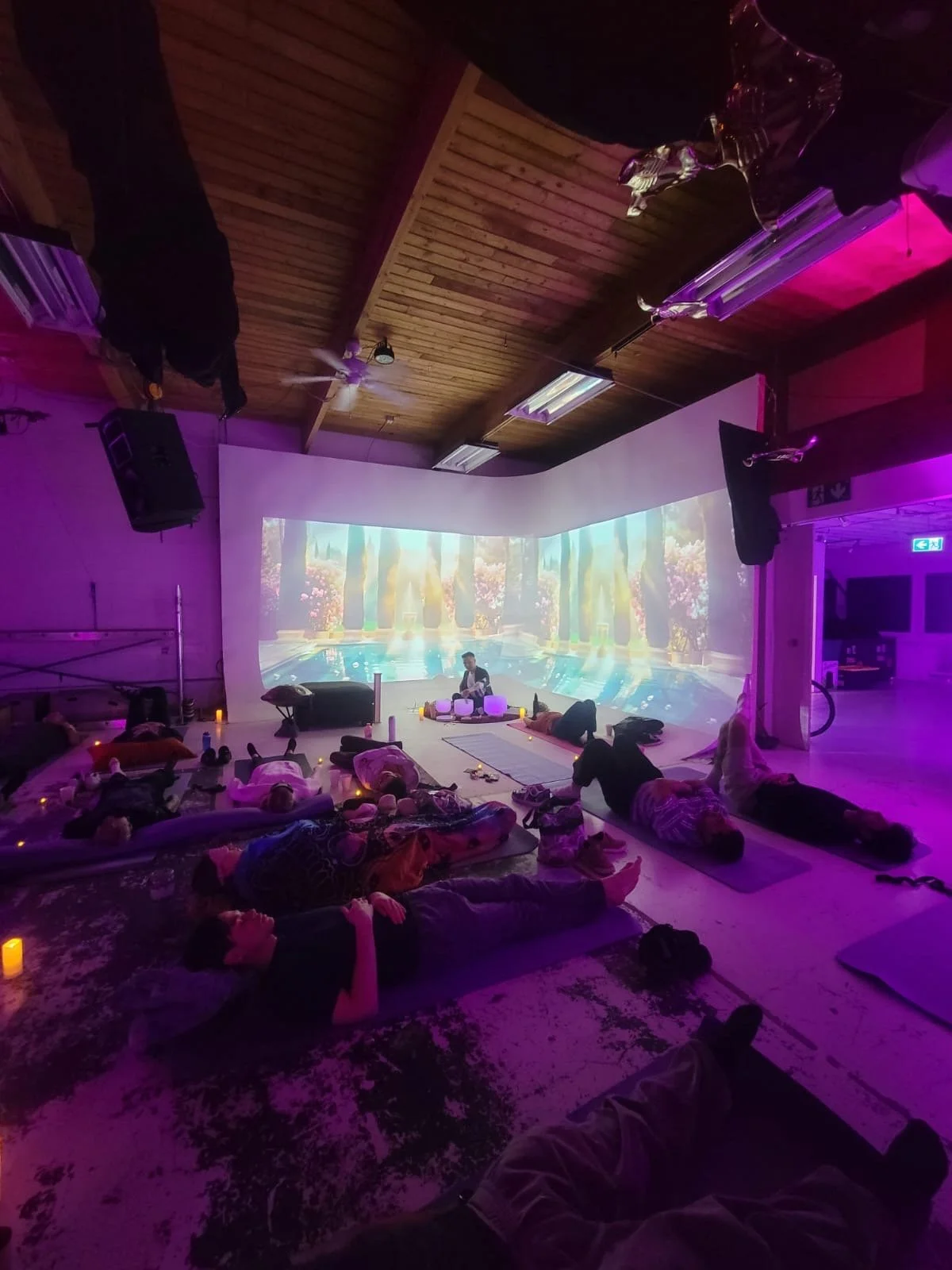Alex Ma performing a public sound bath for relaxed guests in Gastown, Vancouver, BC. With purple lights, candles, and a beautiful backdrop behind him during a Solar Soul Circle event.