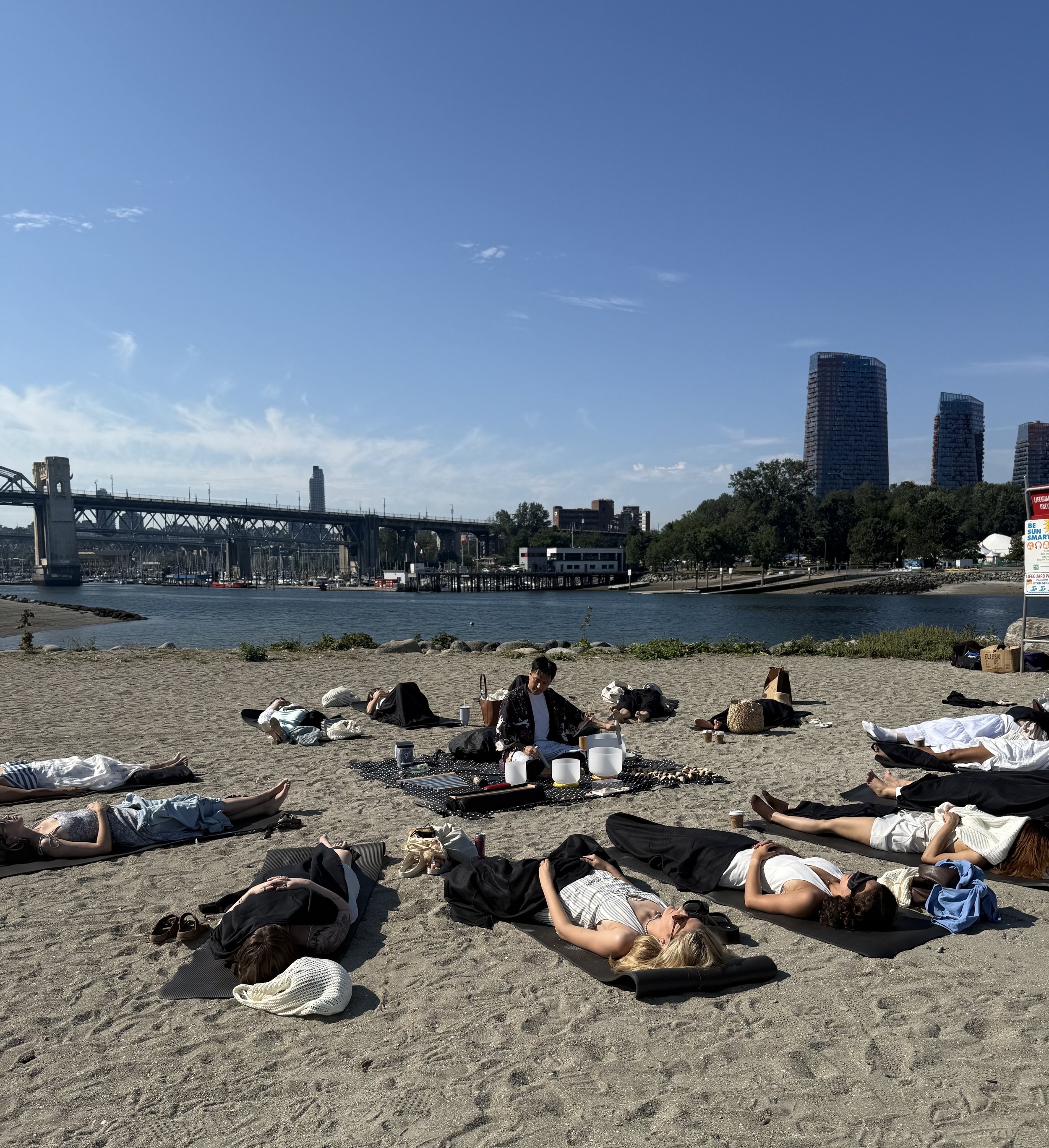 Alex Ma facilitating an outdoor sound bath in Vancouver at Sunset Beach by Solar Soul Circle. For a corporate booking by Olive & Piper Jewelry company.