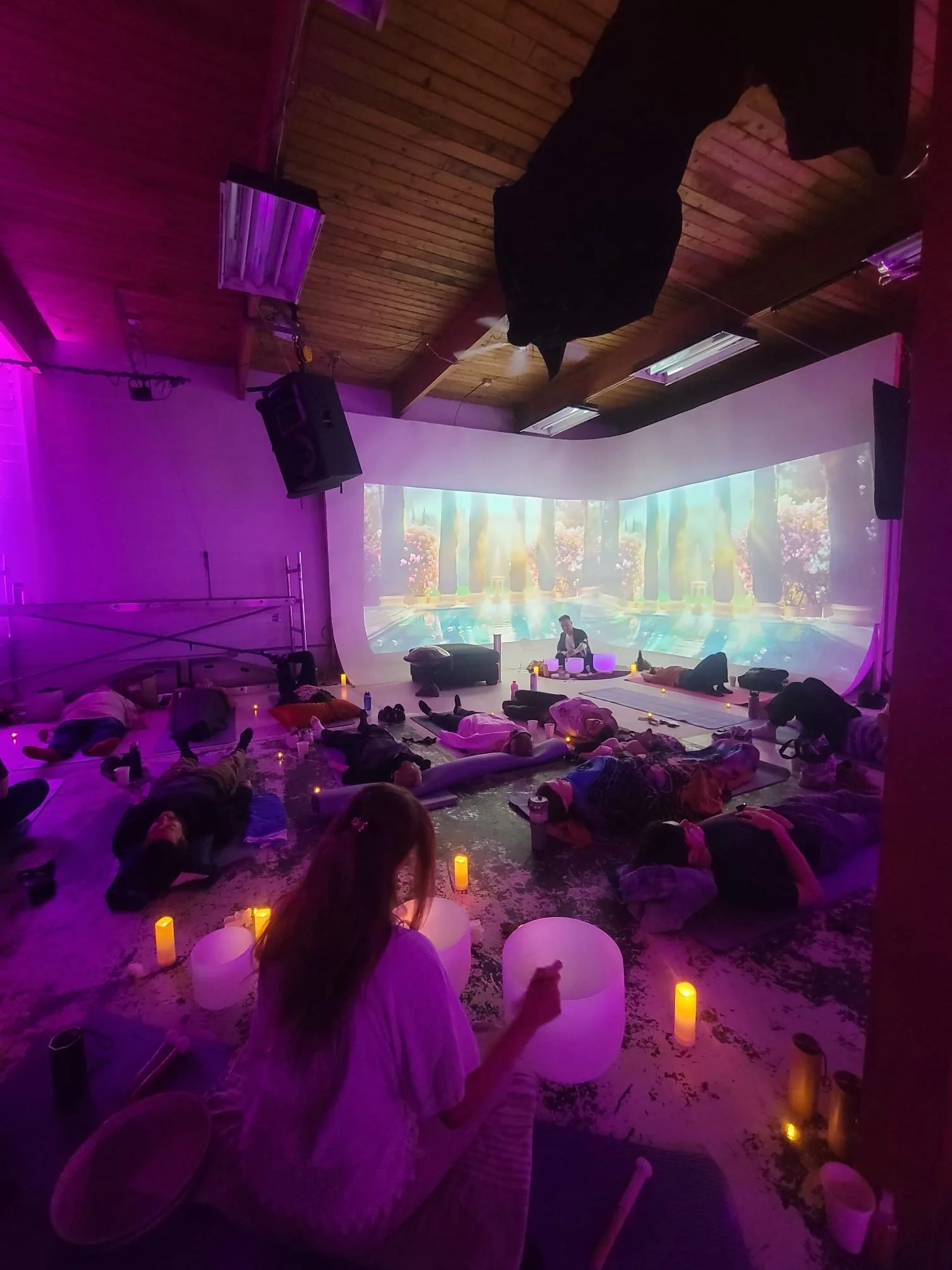 A Solar Soul Circle sound therapy event with Alex Ma and Saja Light performing together in a purple coloured relaxing atmosphere they created lit in candle light while many guests receive sound healing, lying down.