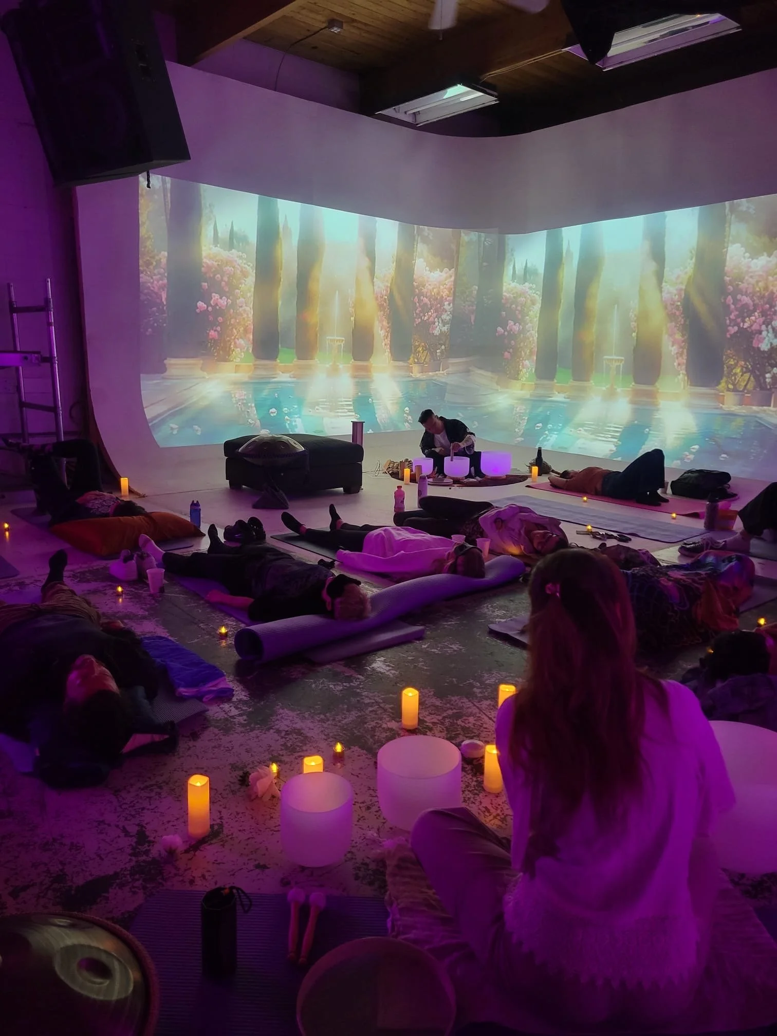 Sound healing session with Alex Ma and Saja Light in collaboration with Samper Caicedo Legacy. Within a space in Gastown, Vancouver, lit with candles, purple lighting and a projected backdrop of fountains. surrounded by Crystal sound bowls they are p