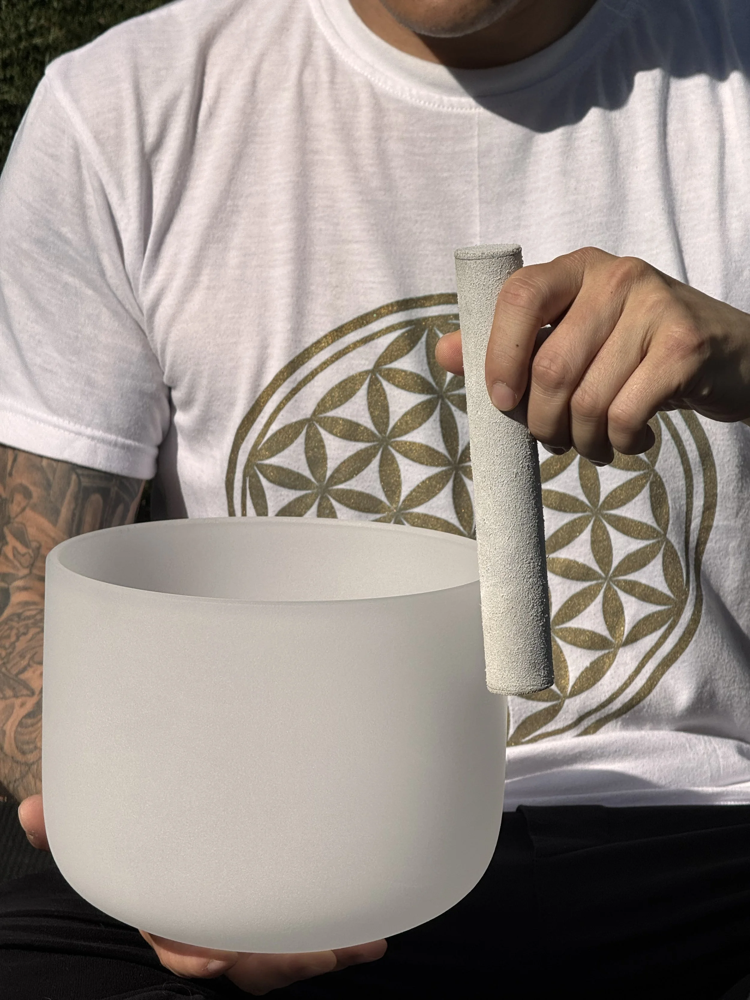 A close up photo of a crystal sound bowl healing session played with a mallet. With a flower of life t shirt in the background in Vancouver.
