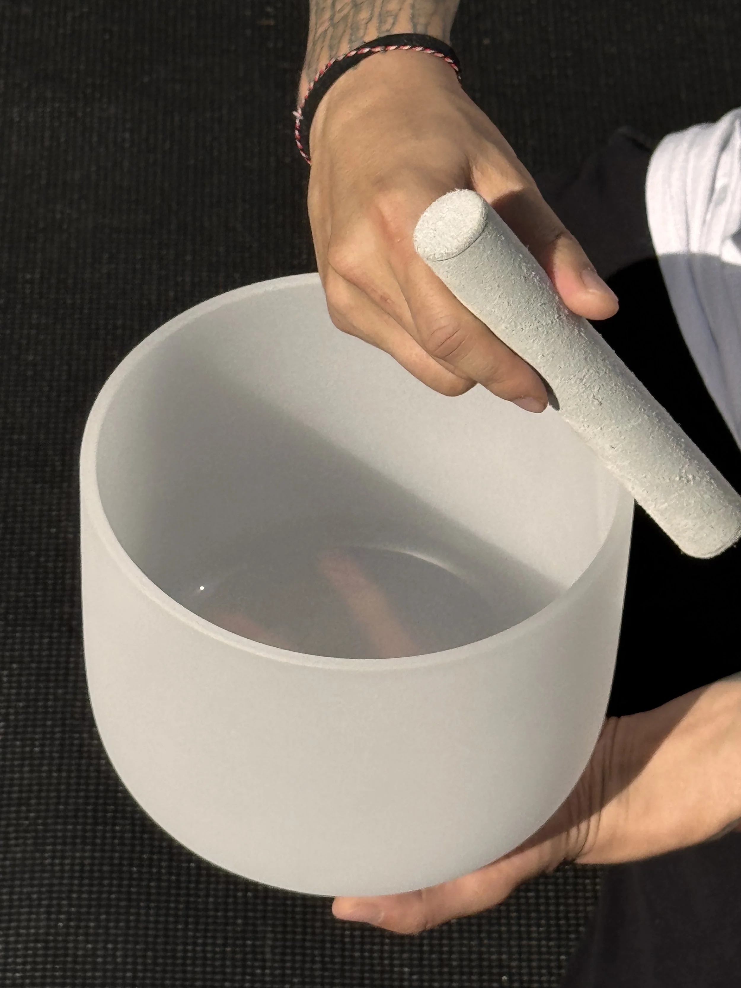 A close up photo of a crystal sound bowl in the note of B being played by Alex Ma of Solar Soul Circle outdoors in Vancouver.