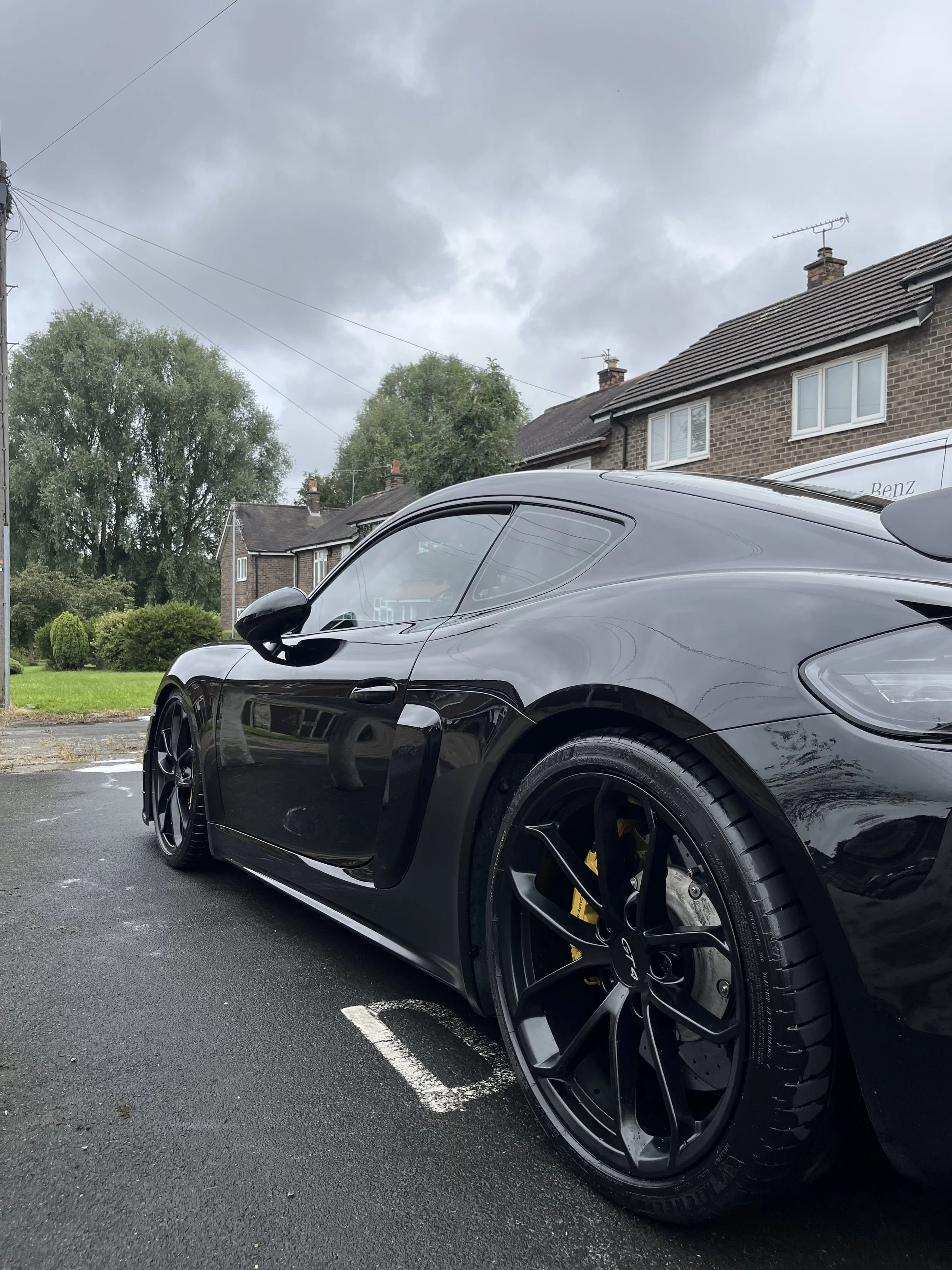 Black sports car parked in a residential area on an overcast day, with houses and trees in the background.