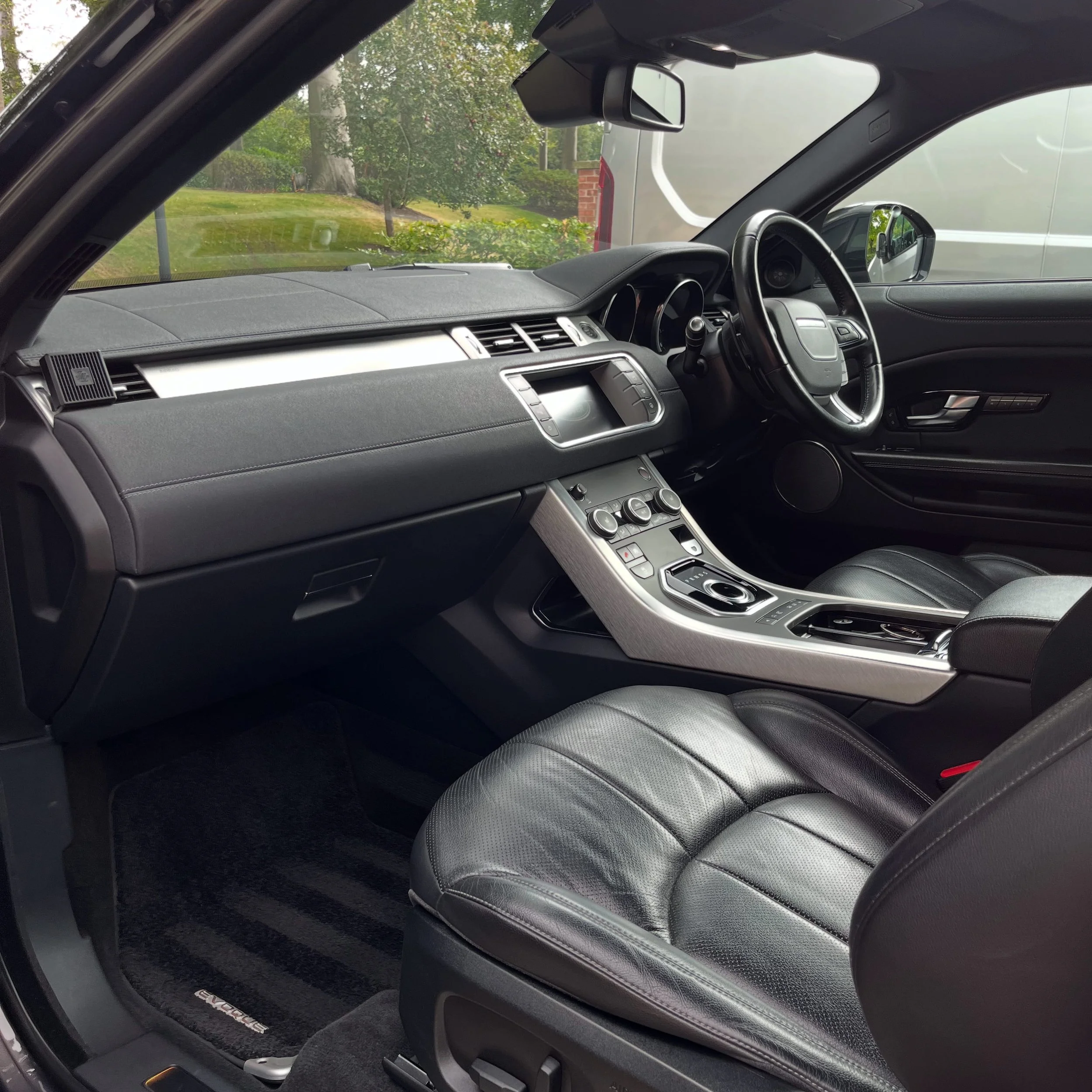 Interior of a luxury car with black leather seats, a sleek dashboard, and a gear shift in the center console, parked outdoors.