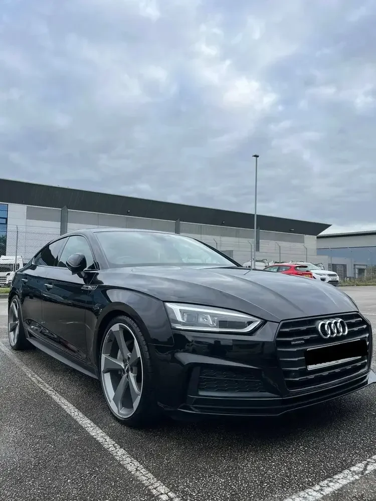 Black Audi sedan parked in a parking lot on a cloudy day.