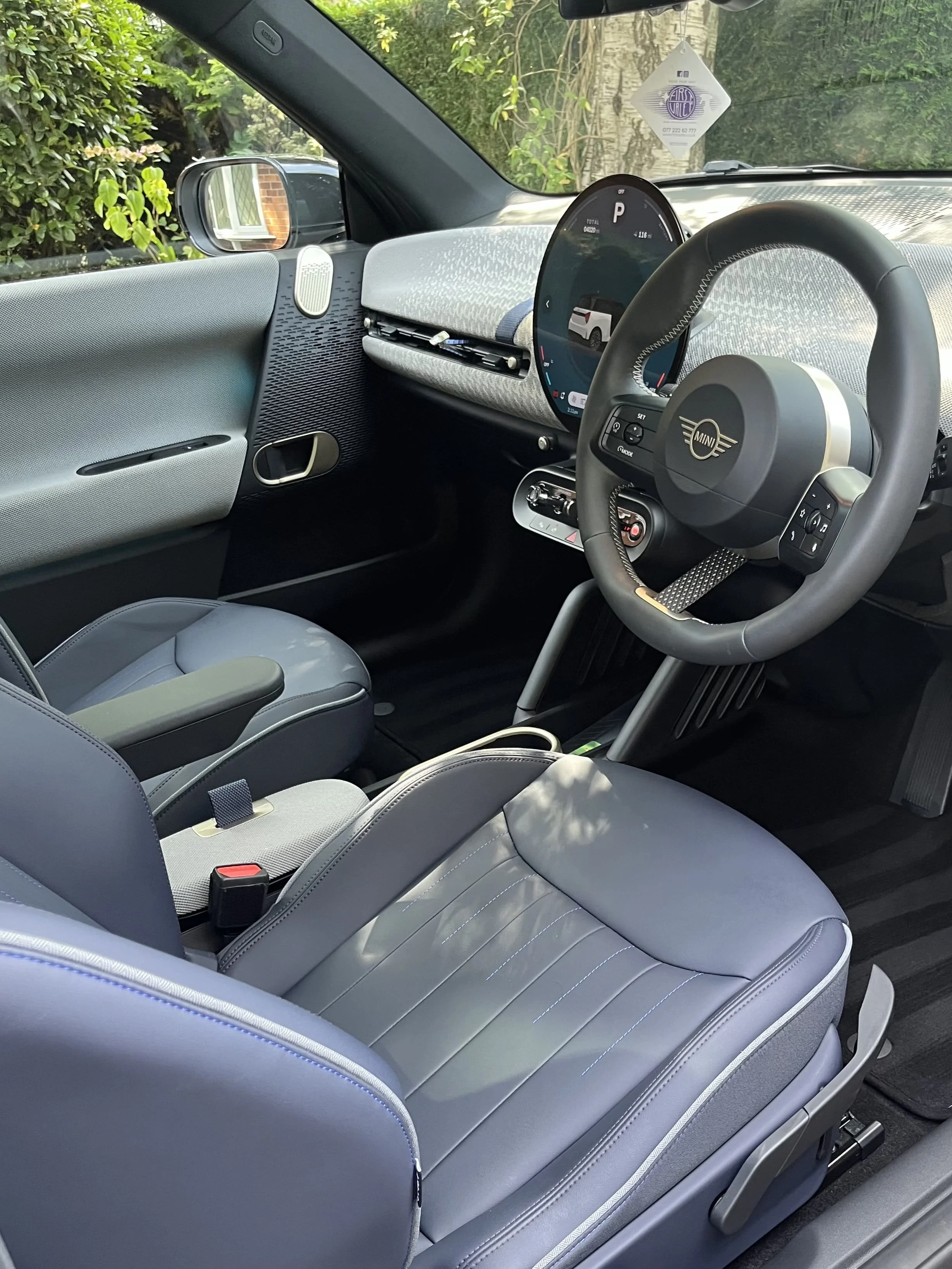 The interior of a modern Mini electric vehicle showing the dashboard, steering wheel, digital instrument cluster, and front passenger seat.