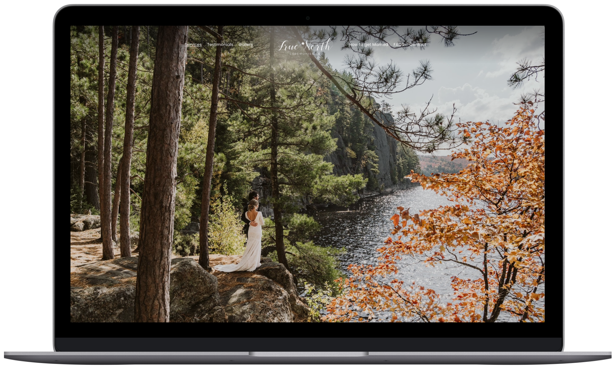 A laptop screen displaying a website with an image of a couple standing by a forested lake, surrounded by trees in autumn colors.