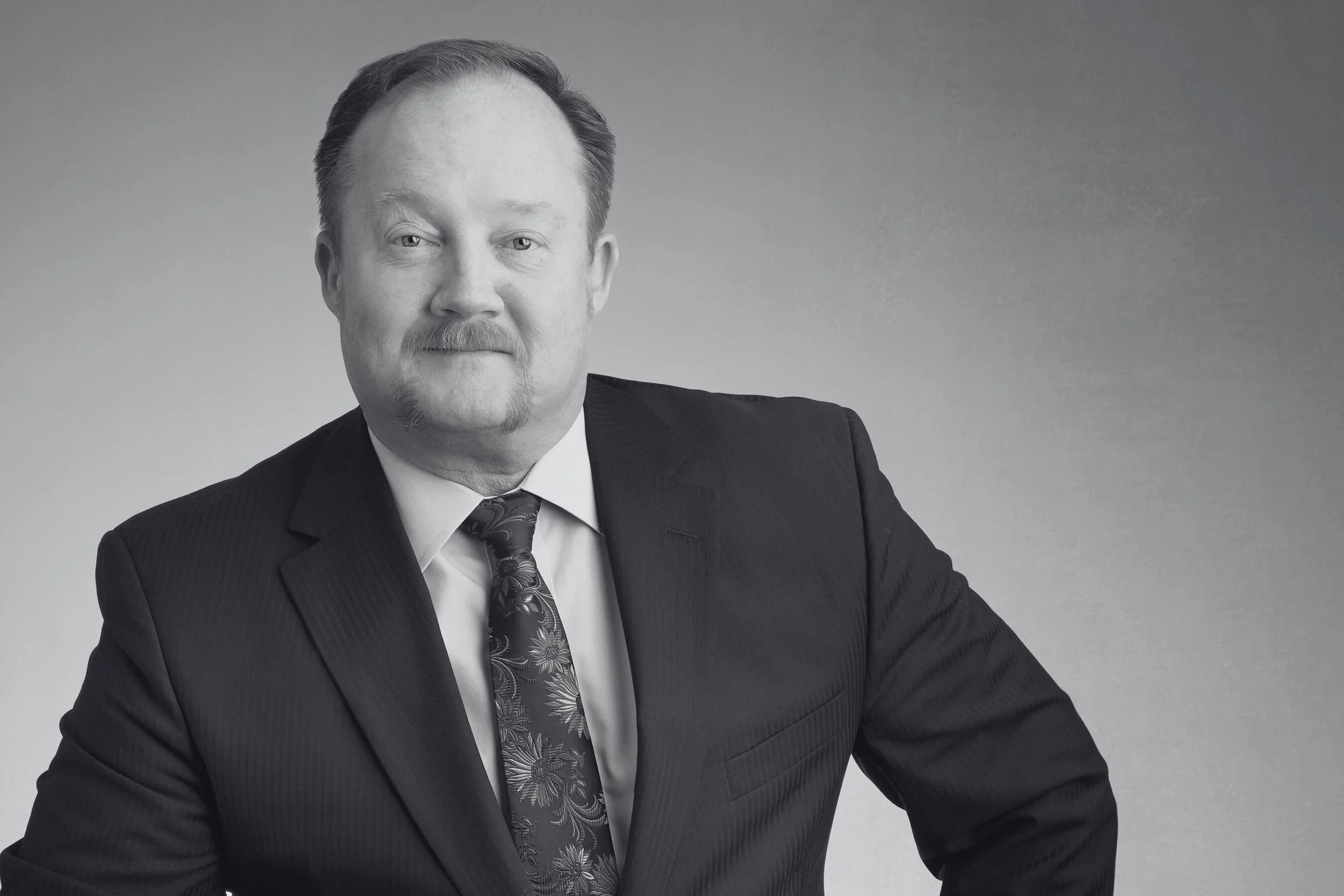 Black and white portrait of a man in a suit, looking confidently at the camera with a hand on his hip.